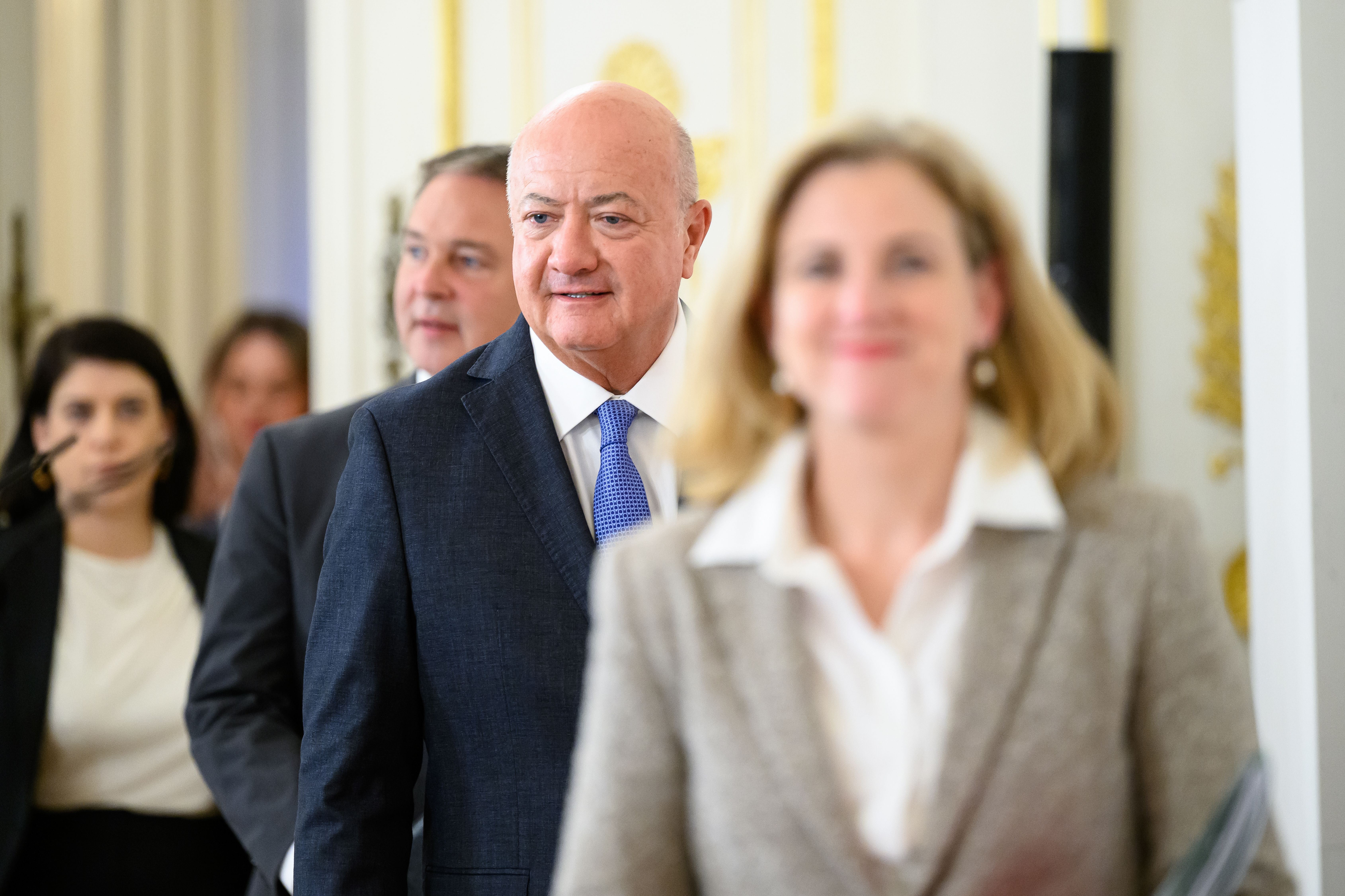 Mehrere Personen im Anzug bei einem Regierungstreffen in einem prunkvollen Raum in Wien.