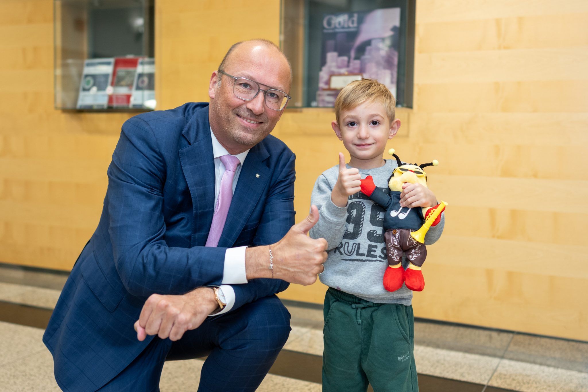 Ein Mann im Anzug und ein Junge mit Plüschbiene zeigen beide den Daumen hoch.