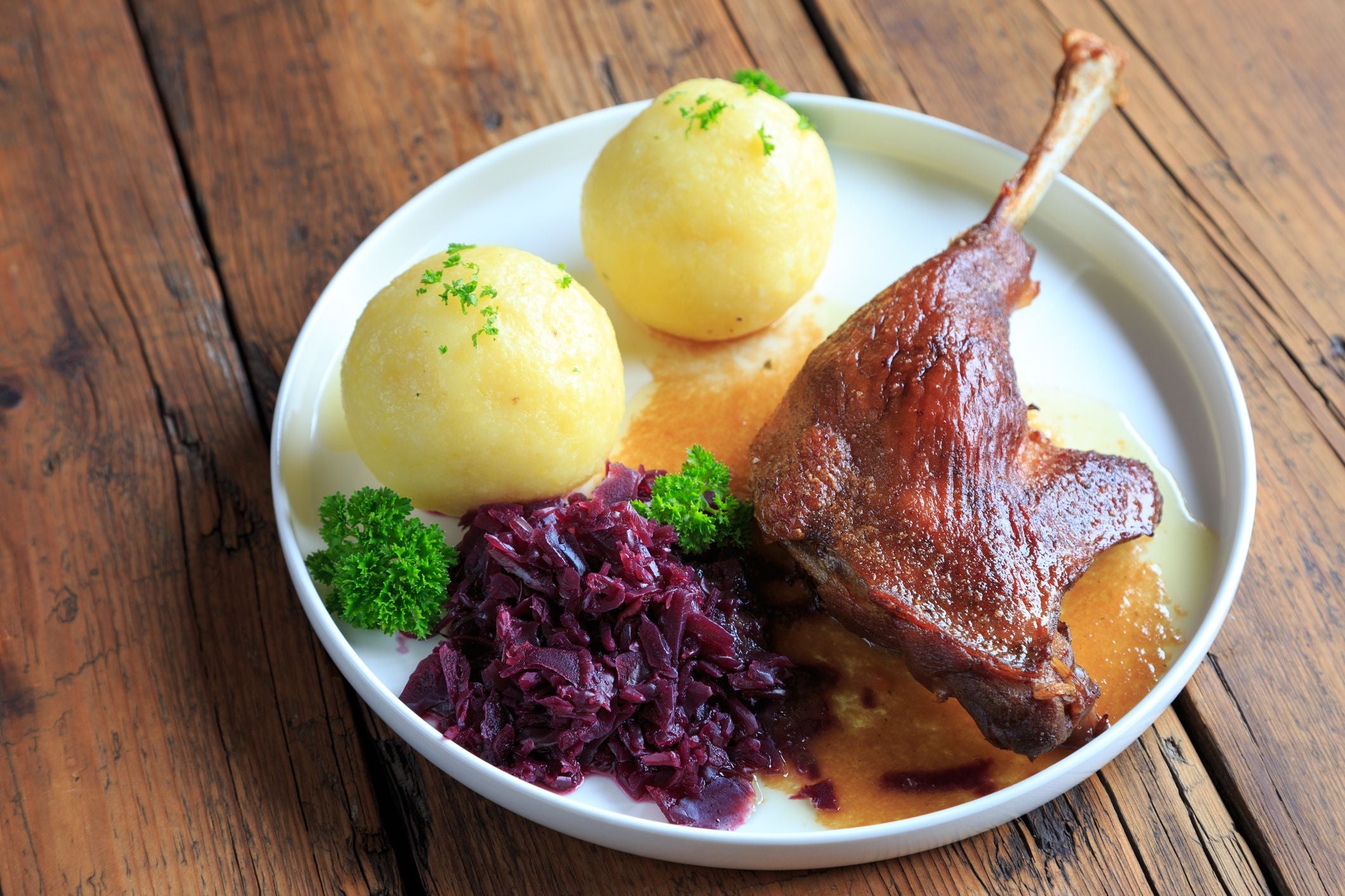 Gebratene Entenkeule mit Rotkohl, zwei Kartoffelklößen und Soße auf einem weißen Teller.