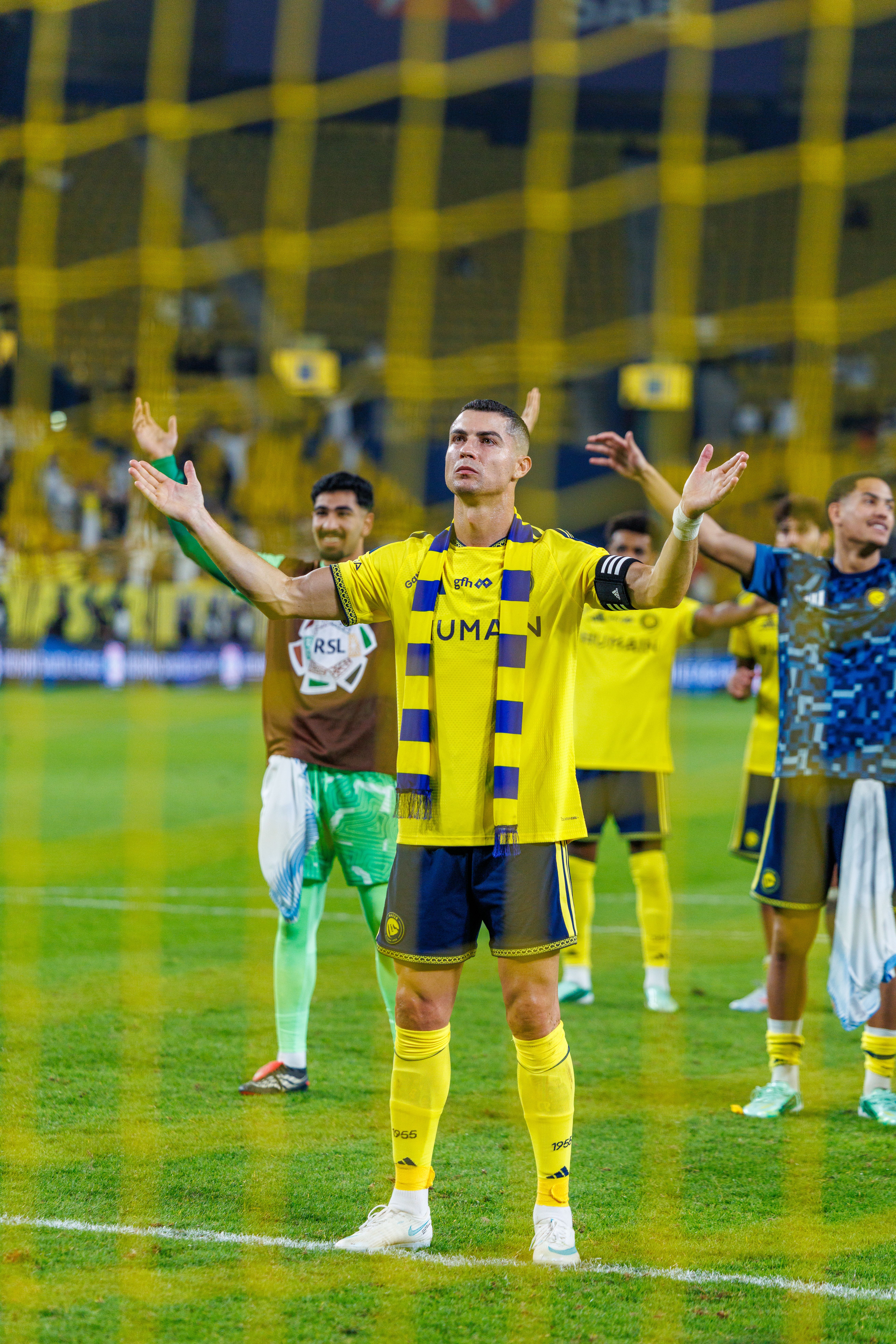 Cristiano Ronaldo breitet im gelben Trikot von Al-Nassr mit einem gelb-blauen Schal um den Hals jubelnd die Arme aus.