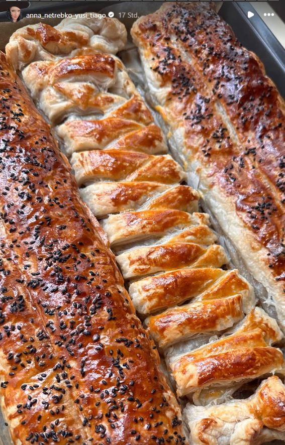 Drei gebackene Blätterteigrollen mit glänzender Oberfläche, teils mit schwarzen Sesam bestreut.