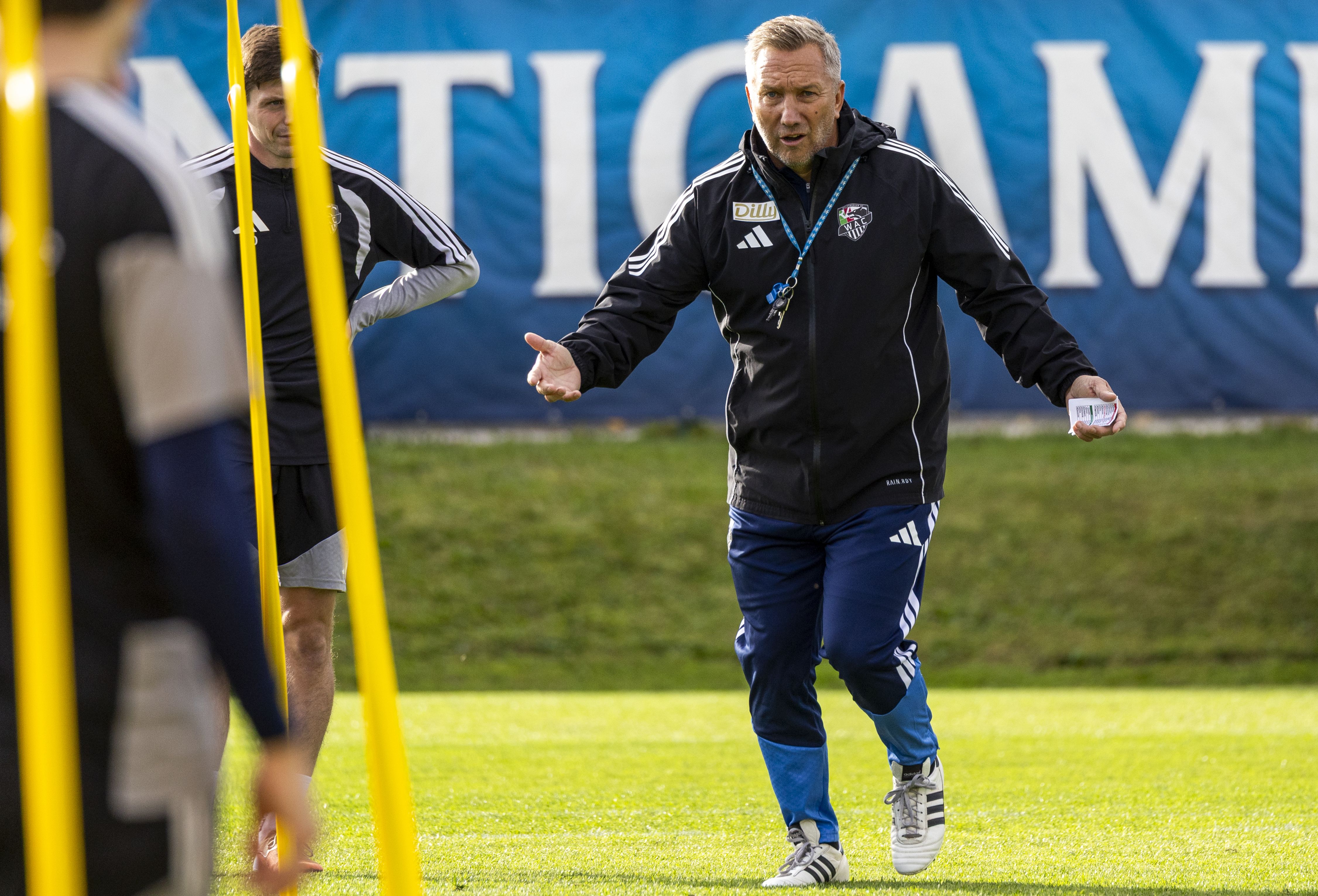 WAC-Trainer Manfred Schmid gestikuliert im schwarzen Trainingsanzug auf dem Trainingsplatz und erklärt engagiert eine Übung.
