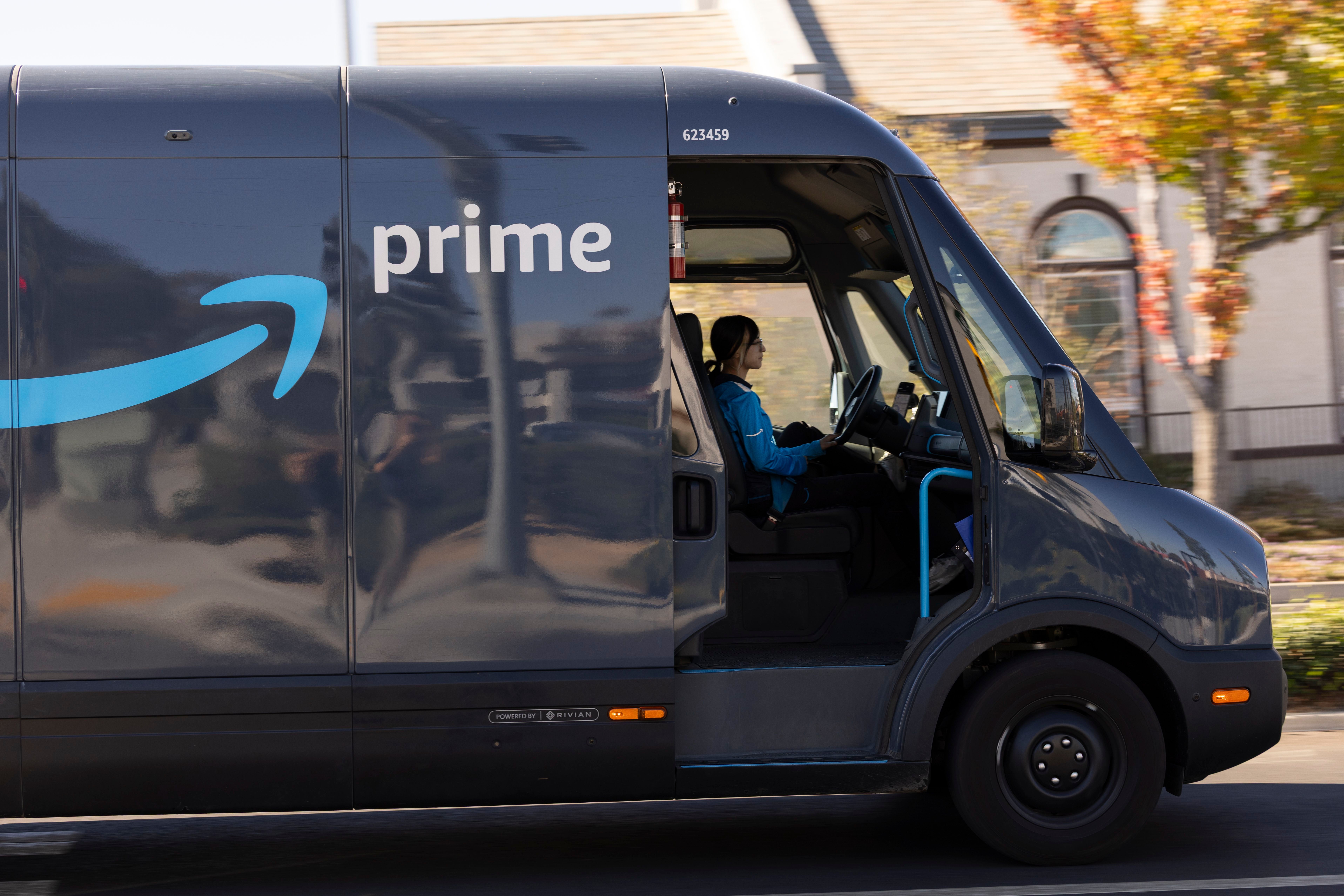 Eine Amazon-Mitarbeiterin fährt einen elektrischen Prime-Lieferwagen durch eine Wohngegend.