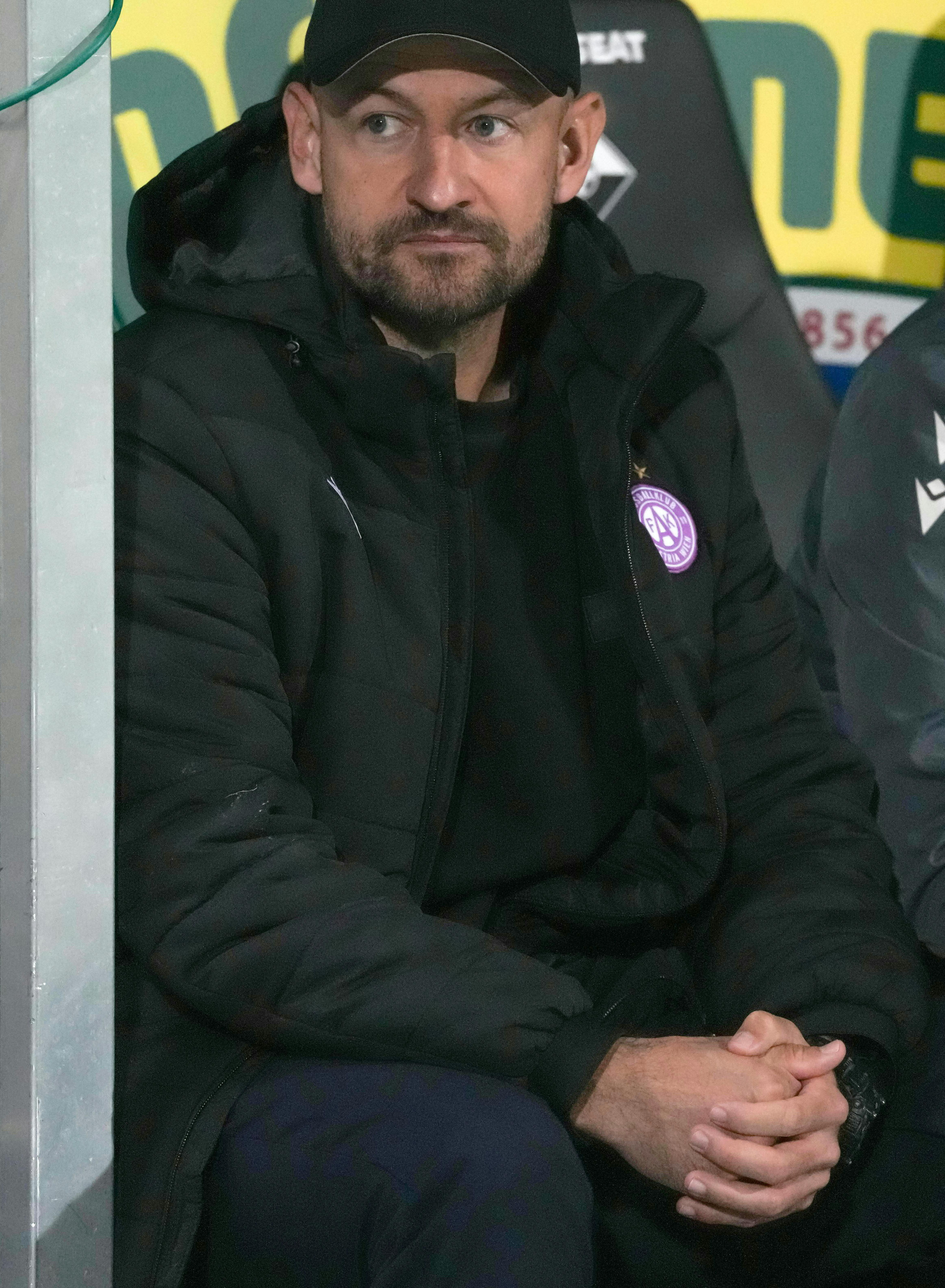 Stephan Helm blickt mit schwarzer Kappe und dunkler Winterjacke nachdenklich von der Trainerbank.