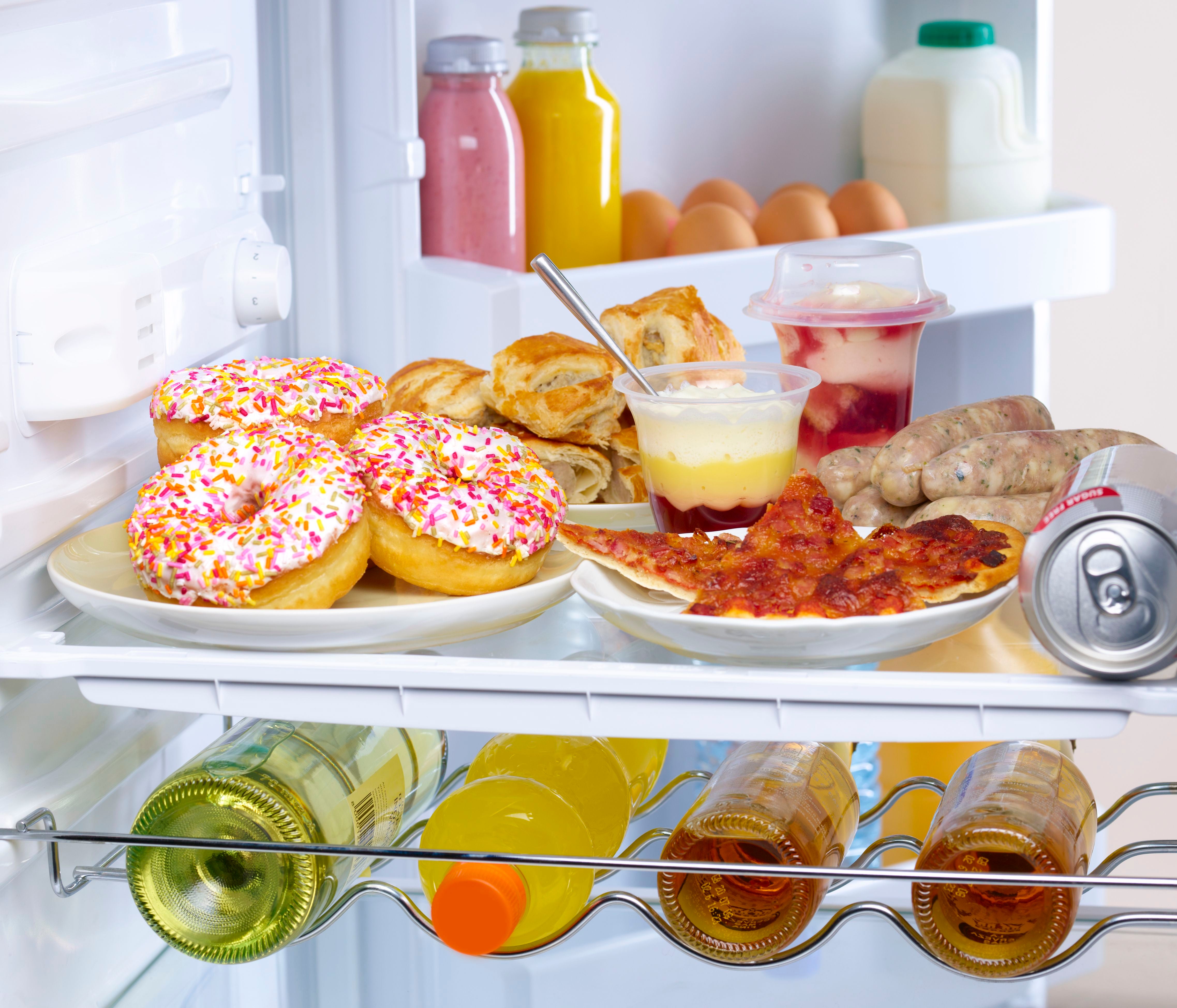 Ein offener Kühlschrank mit Donuts, Pizza, Joghurt, Getränken, Würstchen, Milch und Eiern.