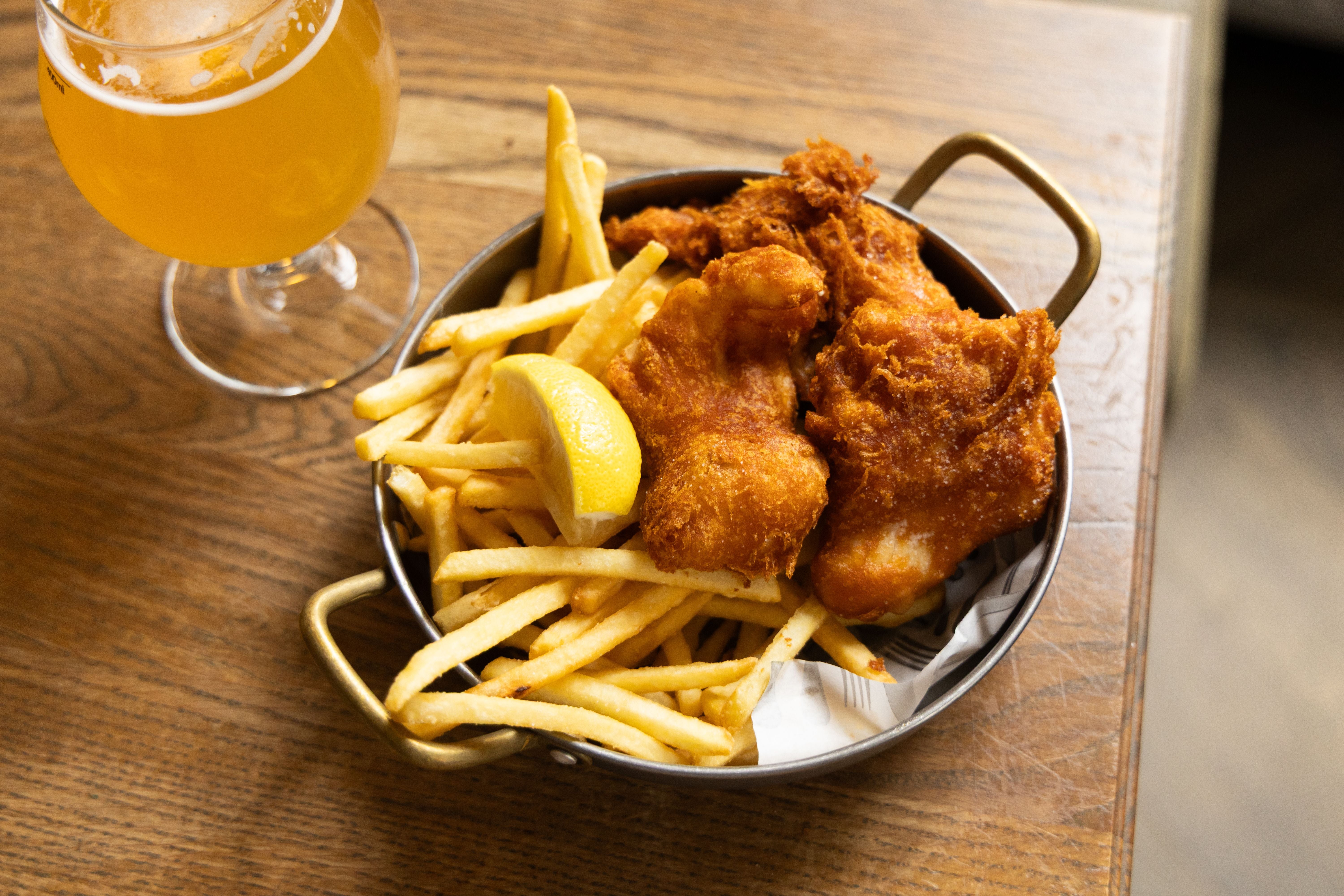 Fish and Chips mit Zitronenspalte und einem Glas Bier auf einem Holztisch serviert.