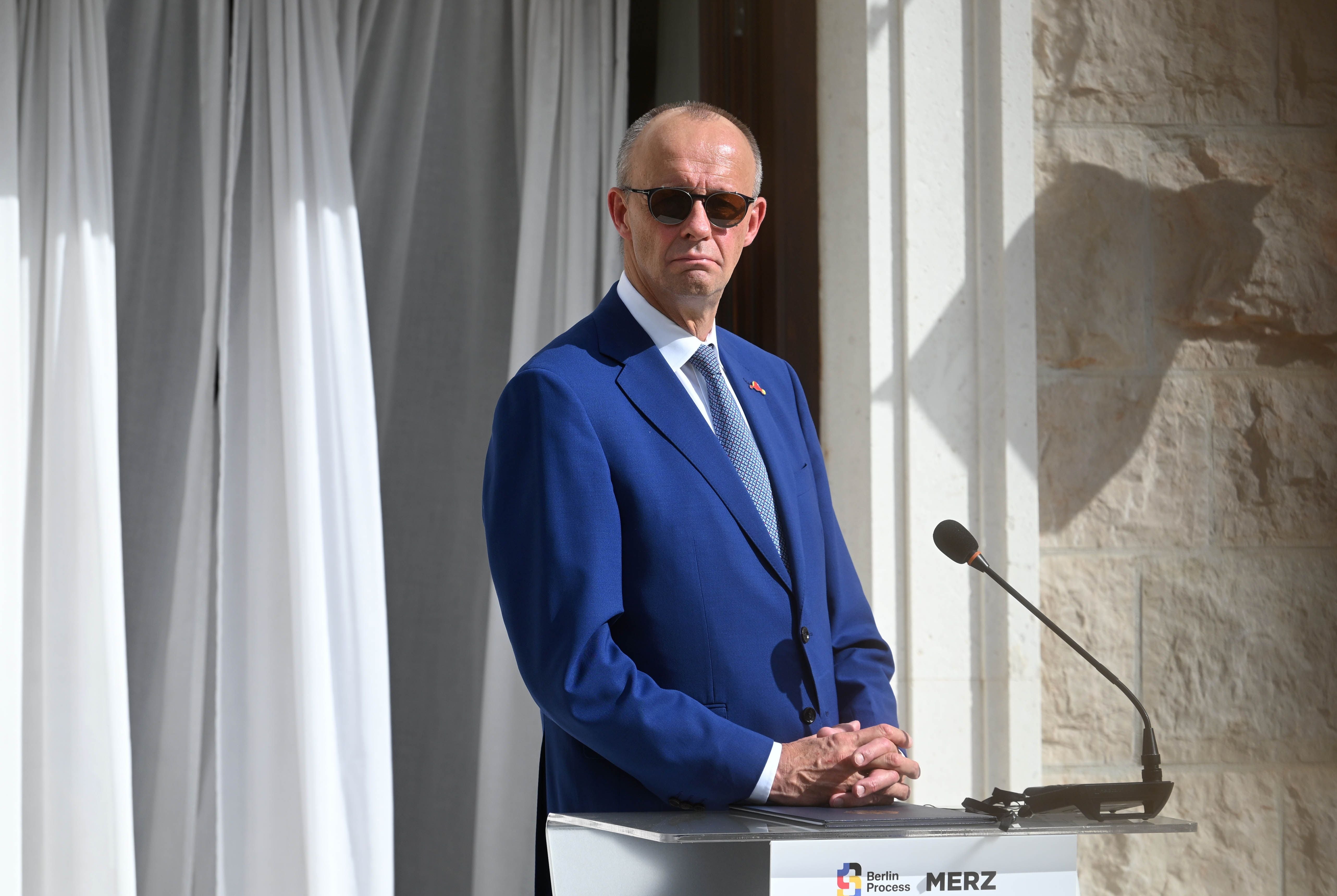 Ein Mann im blauen Anzug steht bei einer Pressekonferenz an einem Pult im Freien.