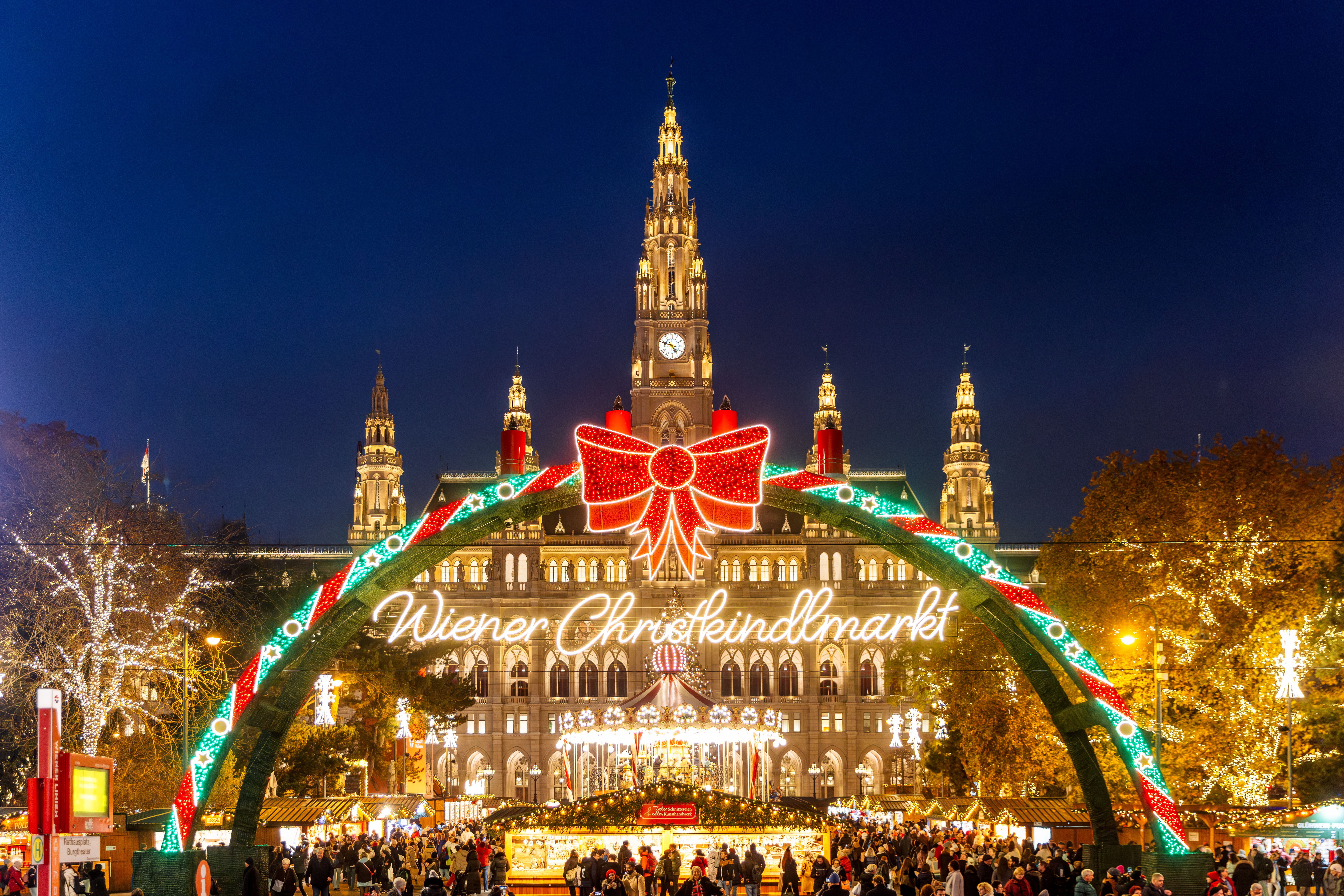 Weihnachtsmarkt am Wiener Rathausplatz mit festlicher Beleuchtung und Menschenmenge bei Nacht.