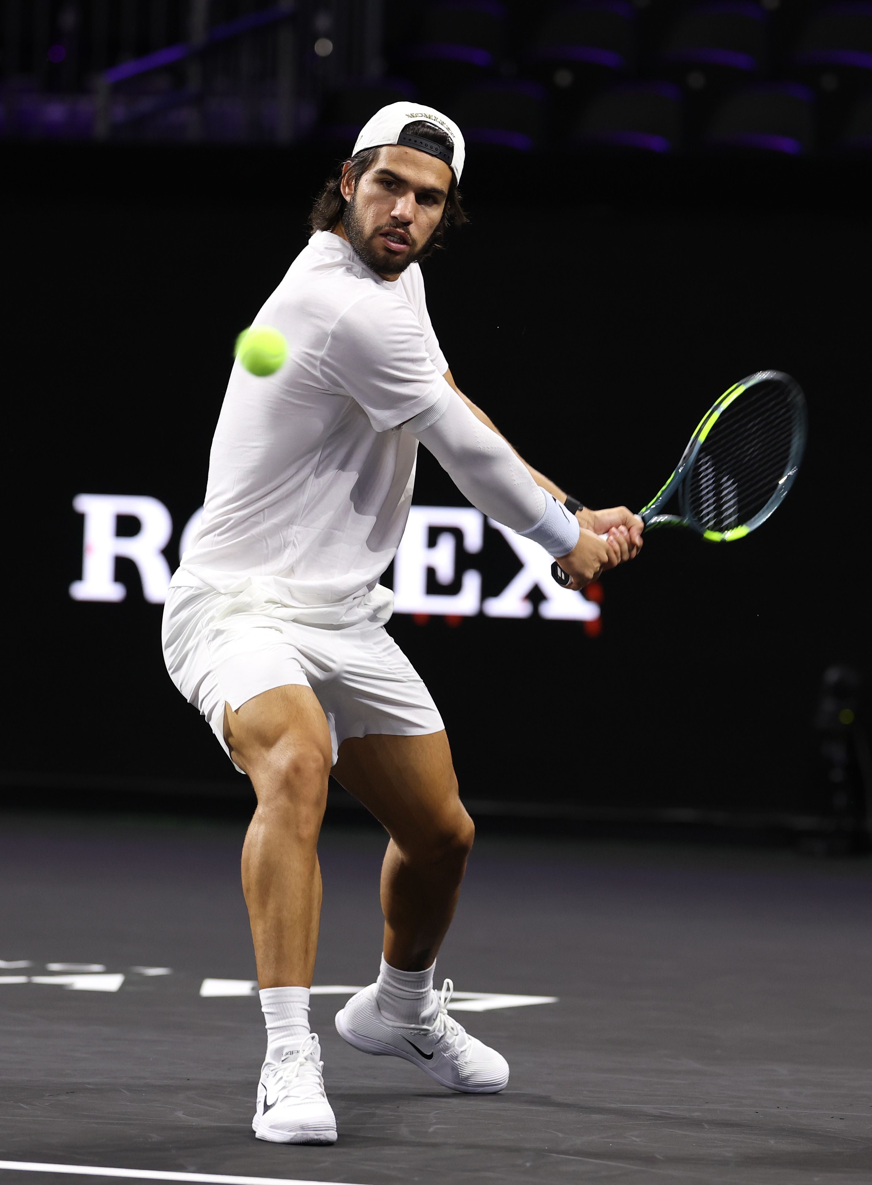 Ein Tennisspieler in Weiß schlägt während eines Trainings eine Rückhand auf einem Hallenplatz.