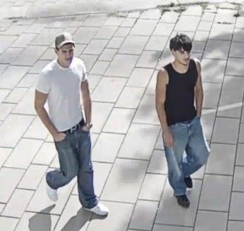 Zwei junge Männer gehen auf einem gepflasterten Gehweg, einer trägt ein weißes T-Shirt, der andere ein schwarzes.