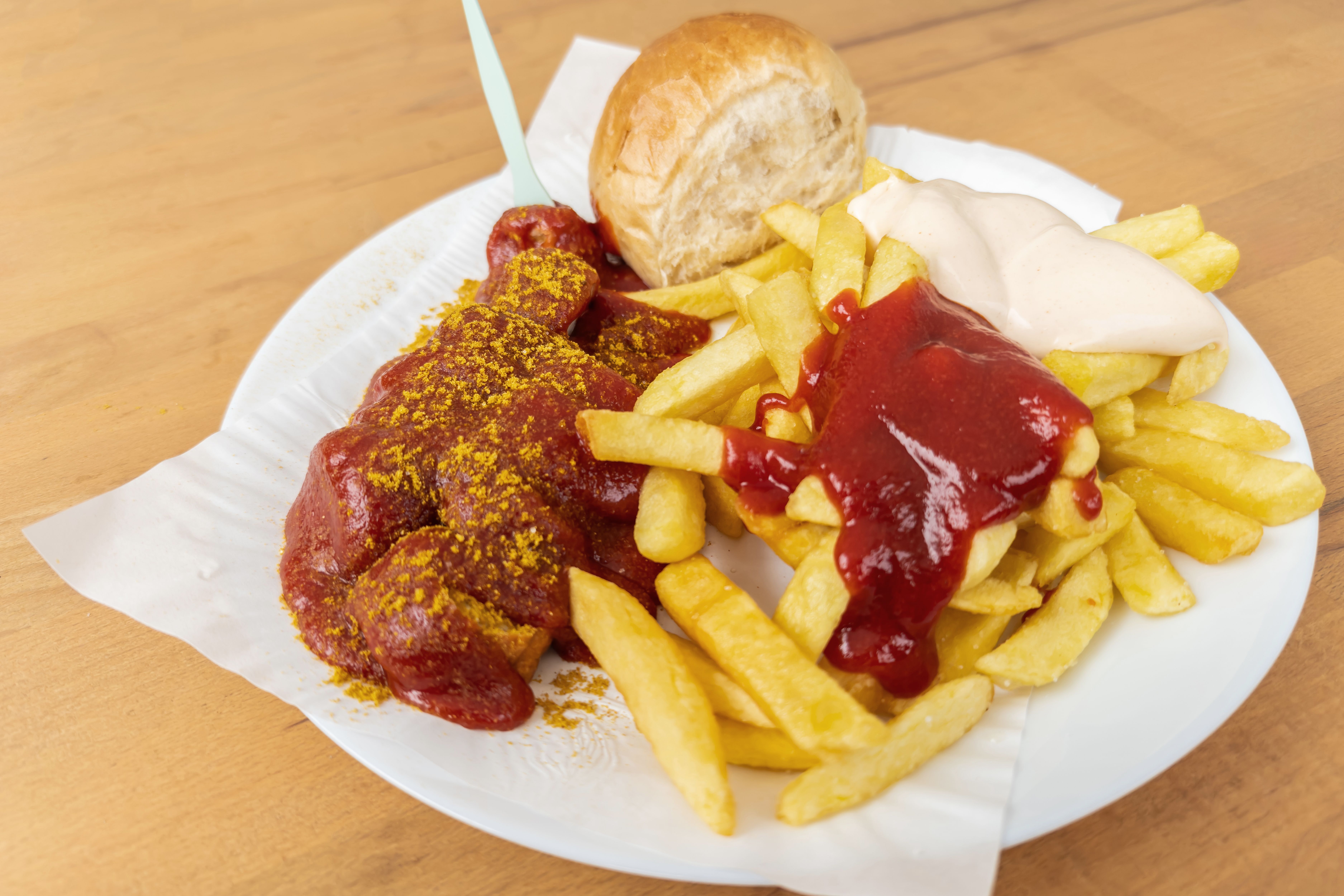 Currywurst mit Pommes, Ketchup, Mayonnaise und Brötchen auf einem Teller.