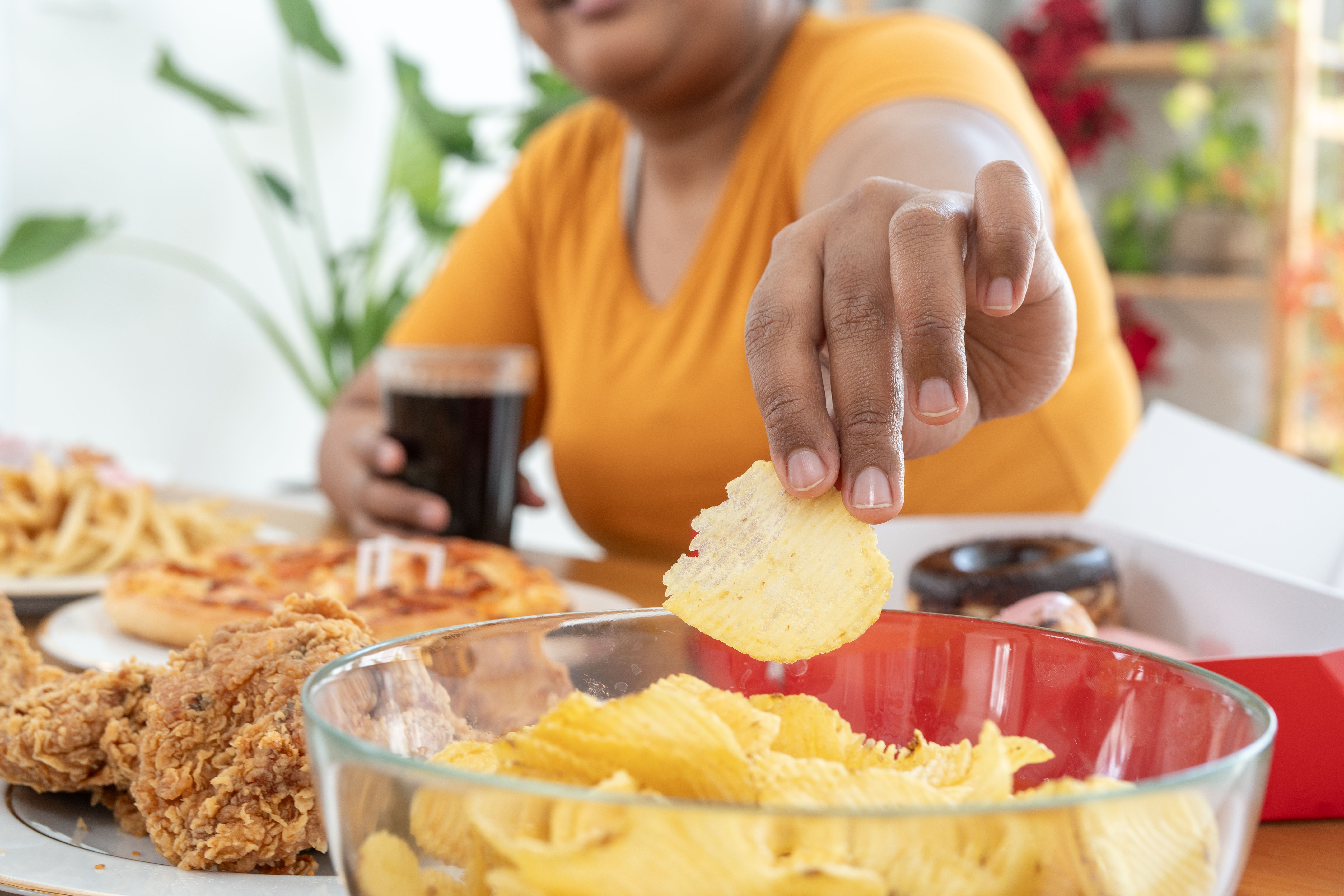 Frau greift zu Kartoffelchips, im Vordergrund frittiertes Essen und Softdrink.