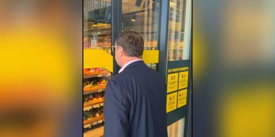 Ein Mann im Anzug betritt einen Supermarkt durch eine automatische Glastür.
