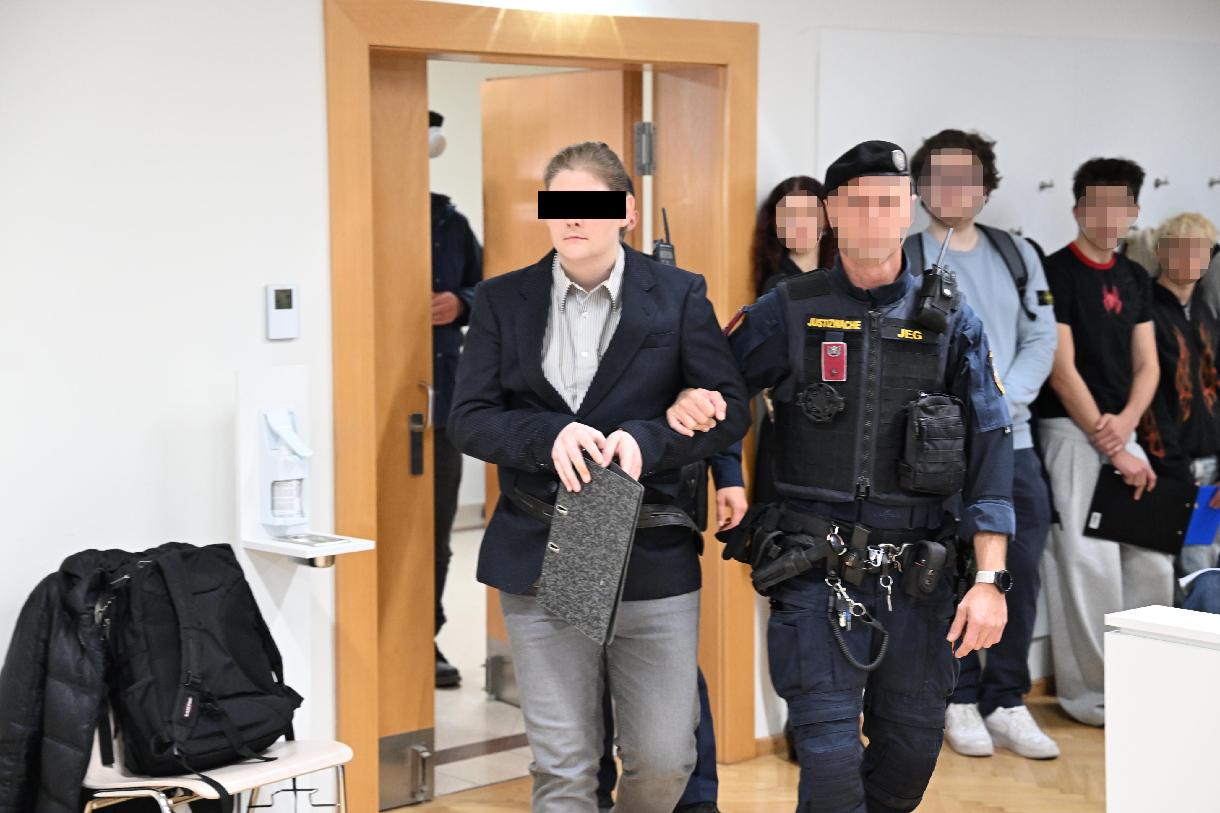 Eine Person wird von einem Justizbeamten in einem Gerichtssaal in Wien begleitet.