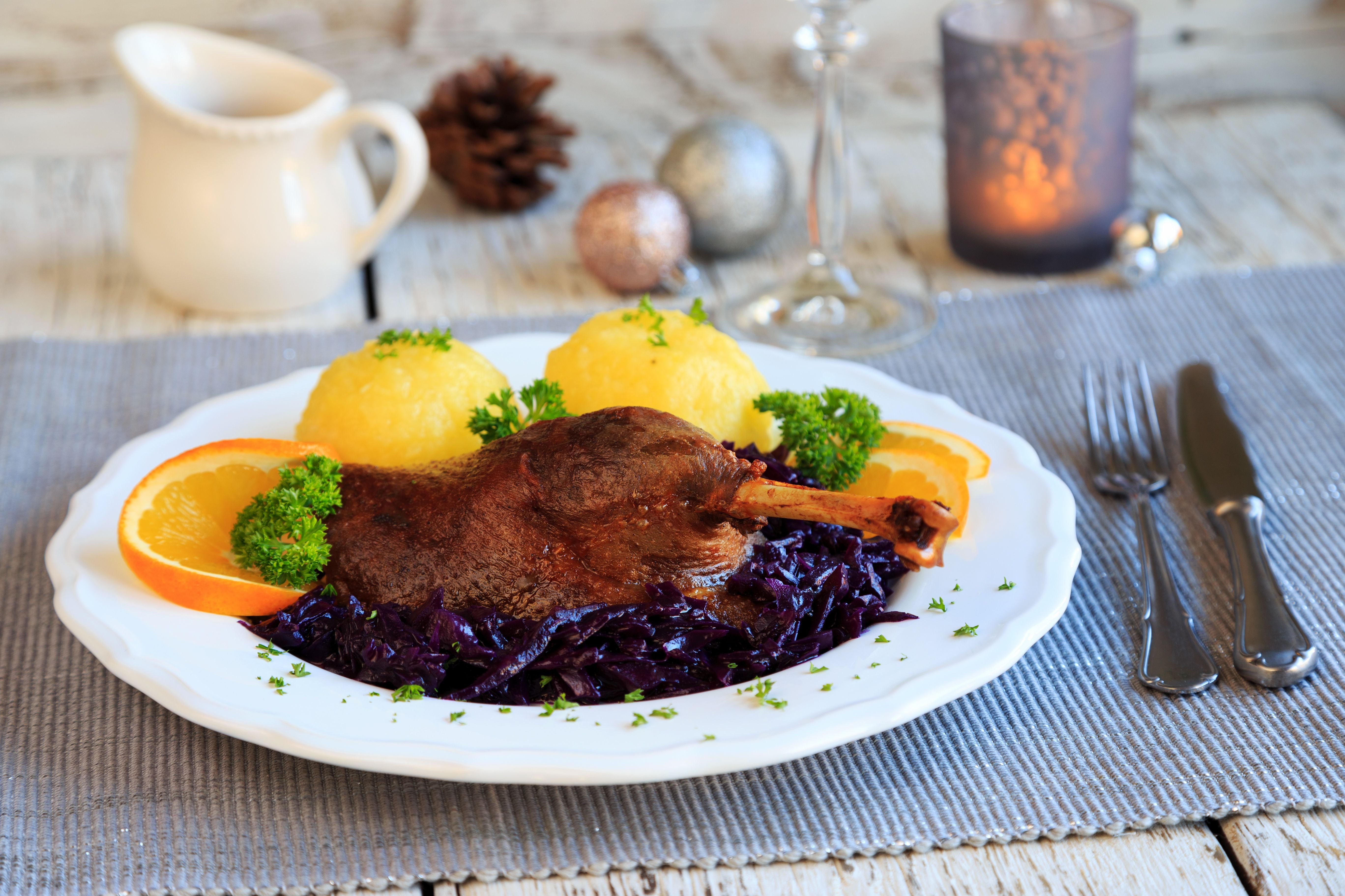 Gebratene Entenkeule mit zwei Klößen, Rotkohl und Orangenscheiben auf einem weißen Teller.