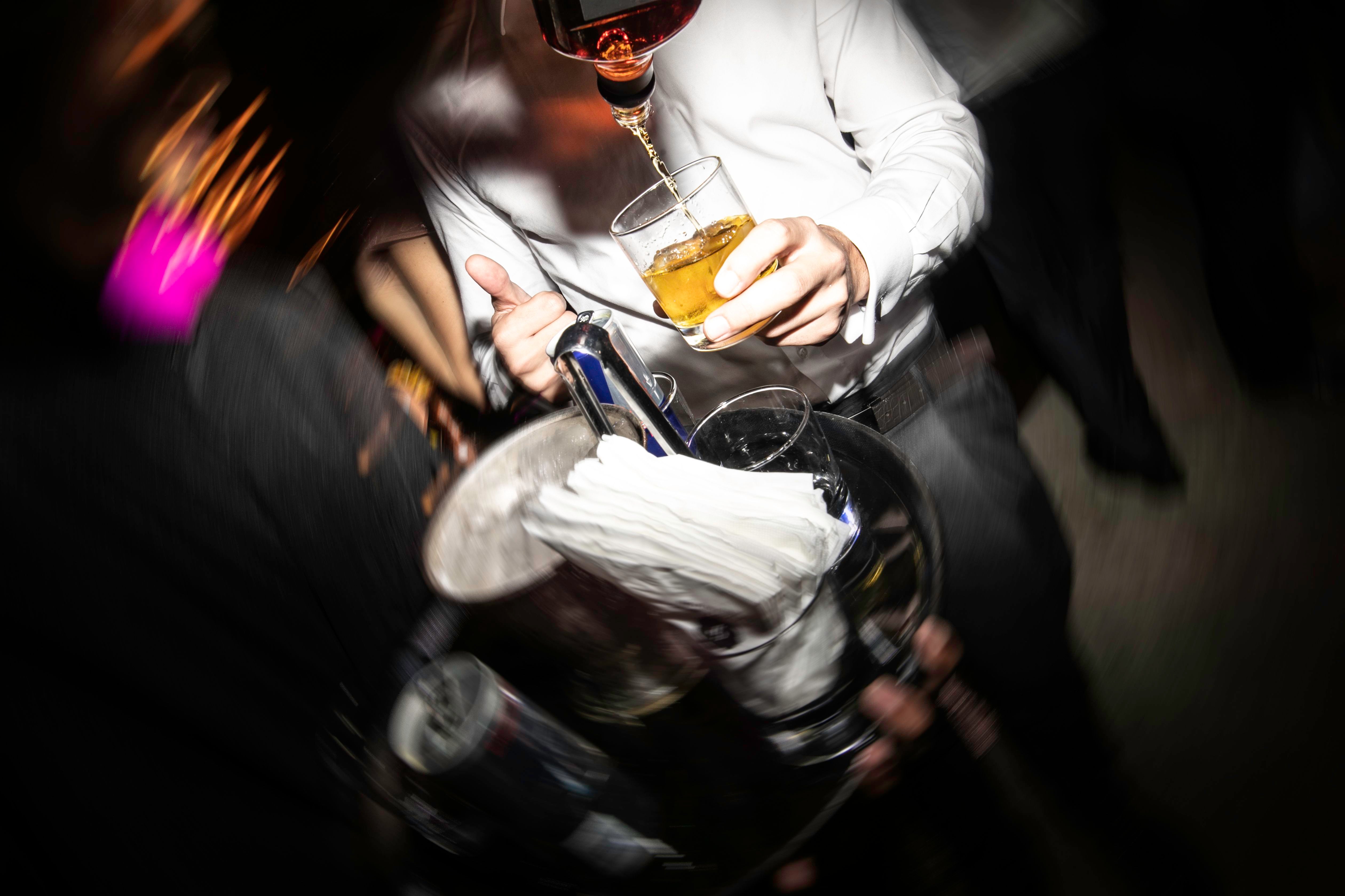 Kellner serviert Getränke auf einem Tablett bei einer Party, Person hält ein Glas Whisky.