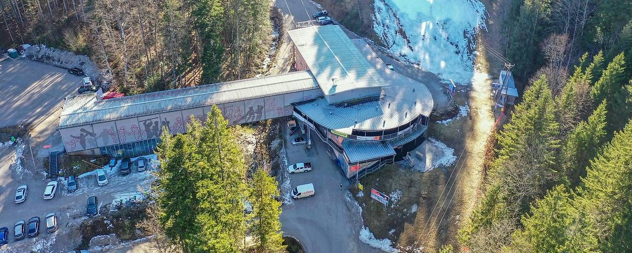 Luftaufnahme einer Bergstation im Skigebiet Kasberg mit parkenden Autos und schneebedecktem Hang.