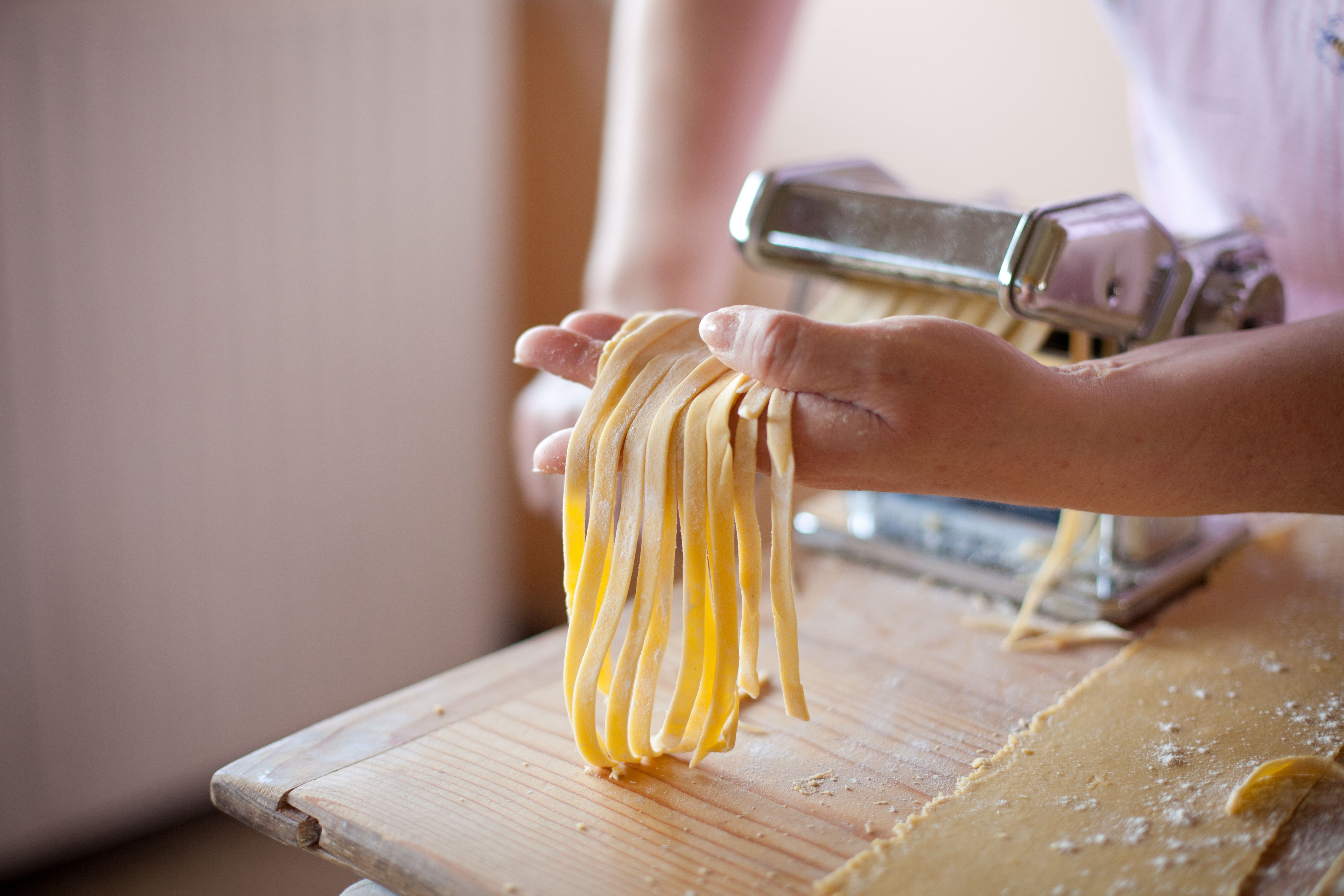 Hände halten frische Tagliatelle, die mit einer Nudelmaschine gemacht wurden.