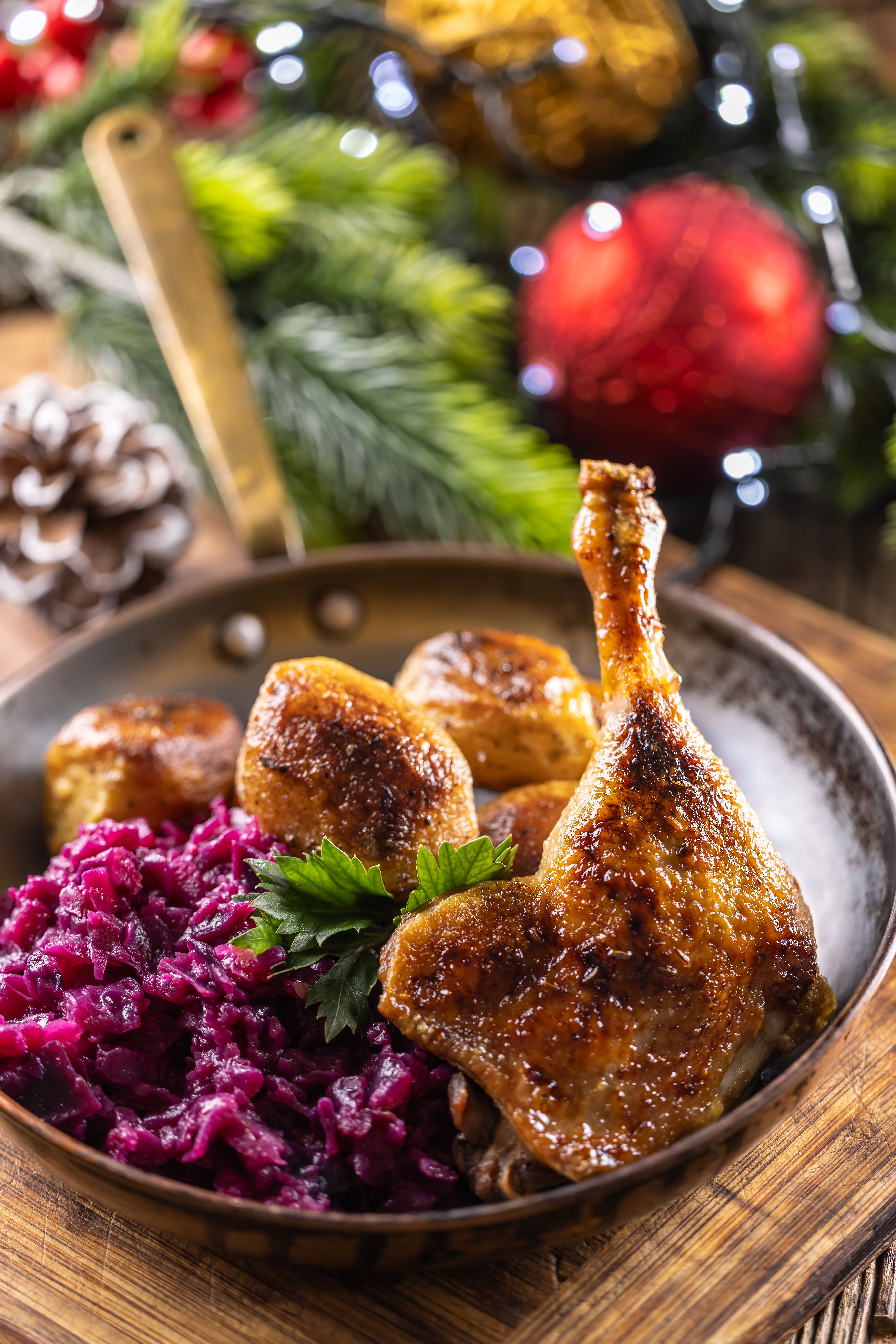 Gebratene Entenkeule mit Rotkohl und Kartoffeln in einer Pfanne, weihnachtlich dekoriert.