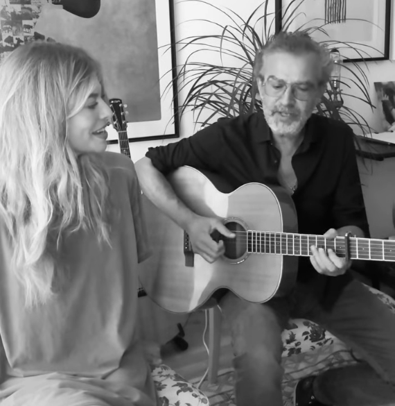 Ein Mann spielt Gitarre, eine Frau sitzt neben ihm und beide scheinen gemeinsam zu musizieren.