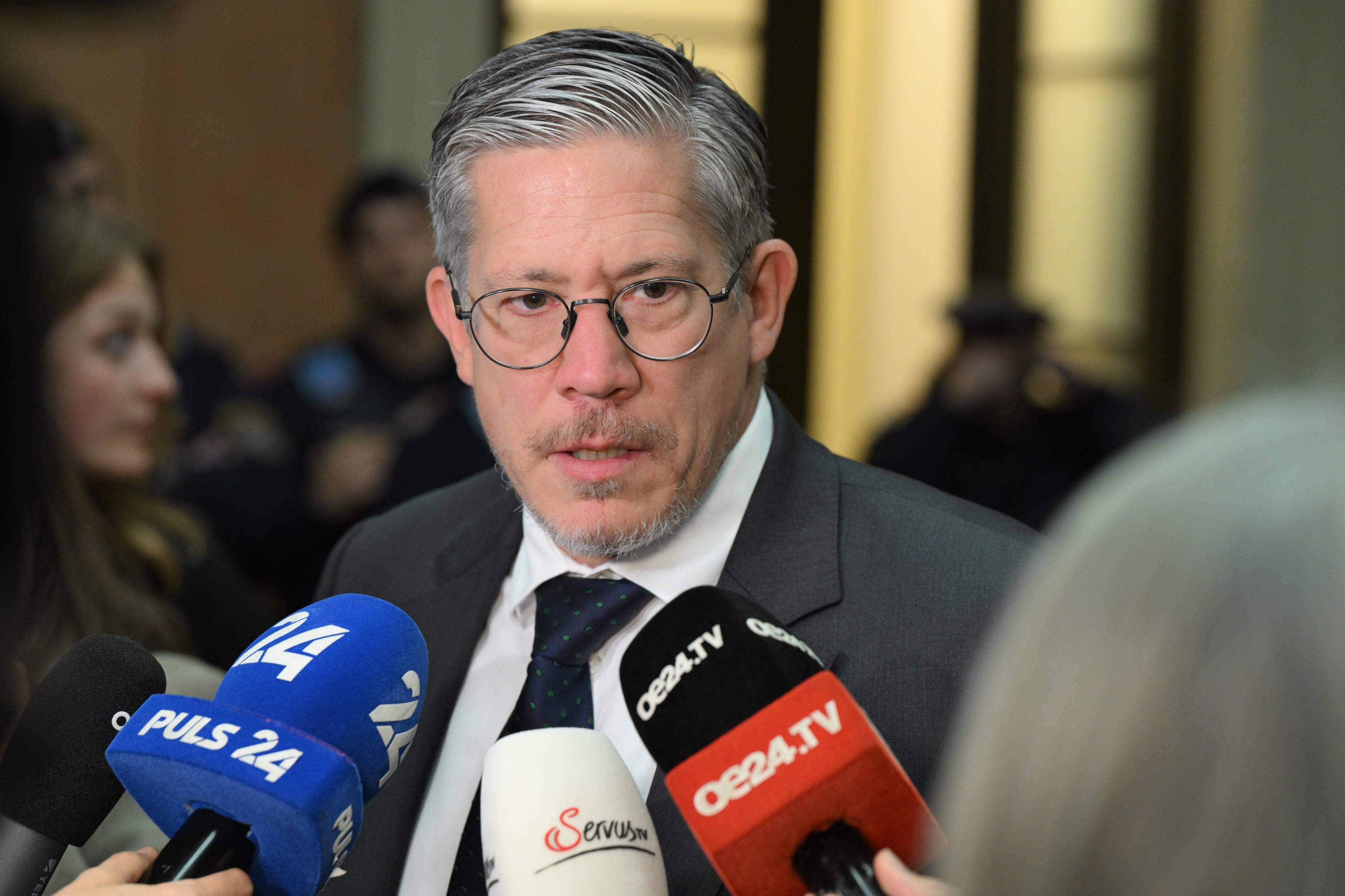 Ein Mann im Anzug spricht vor mehreren Mikrofonen verschiedener TV-Sender mit der Presse.