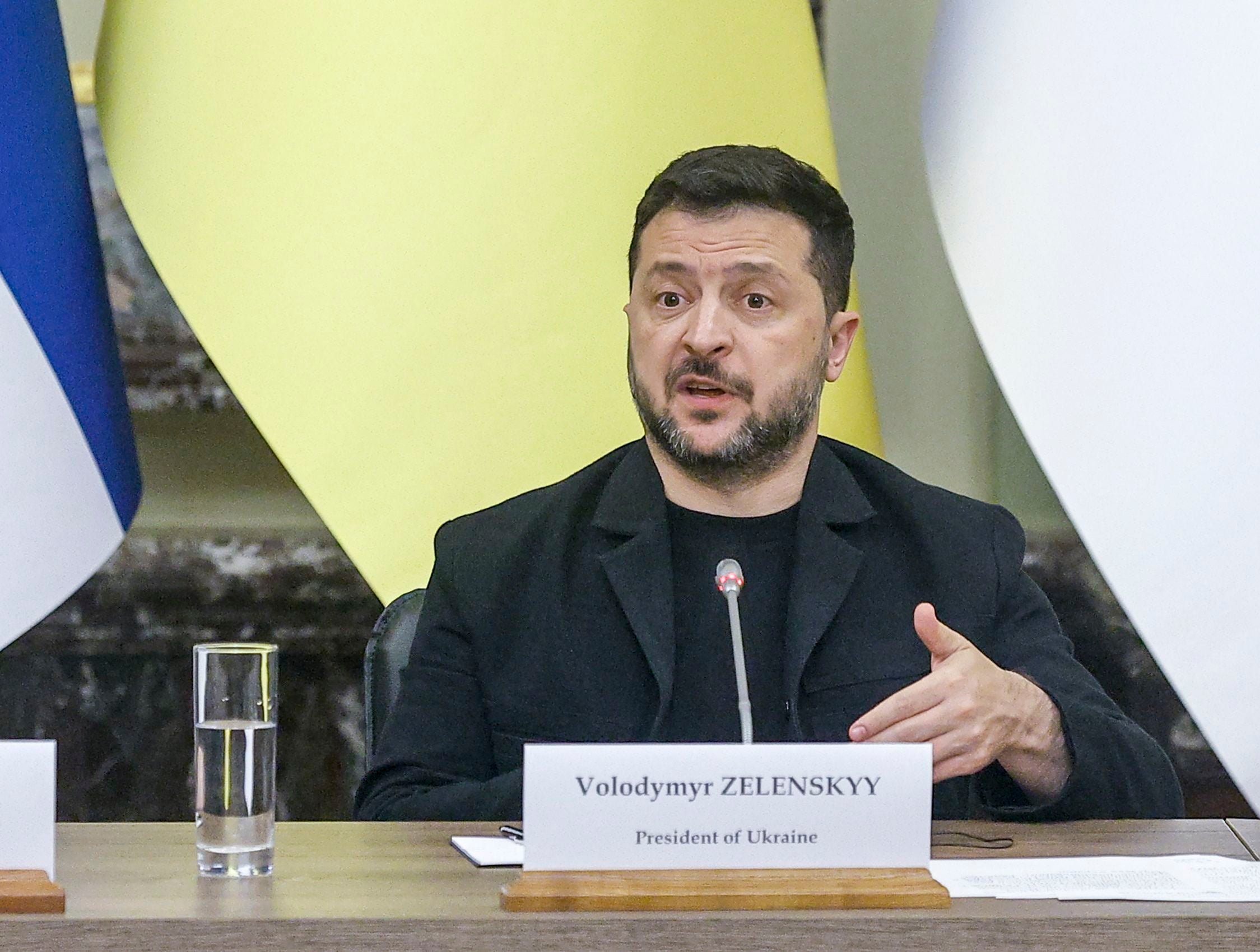 Der ukrainische Präsident Selenskyj spricht auf einer Pressekonferenz mit Mikrofon und Namensschild.