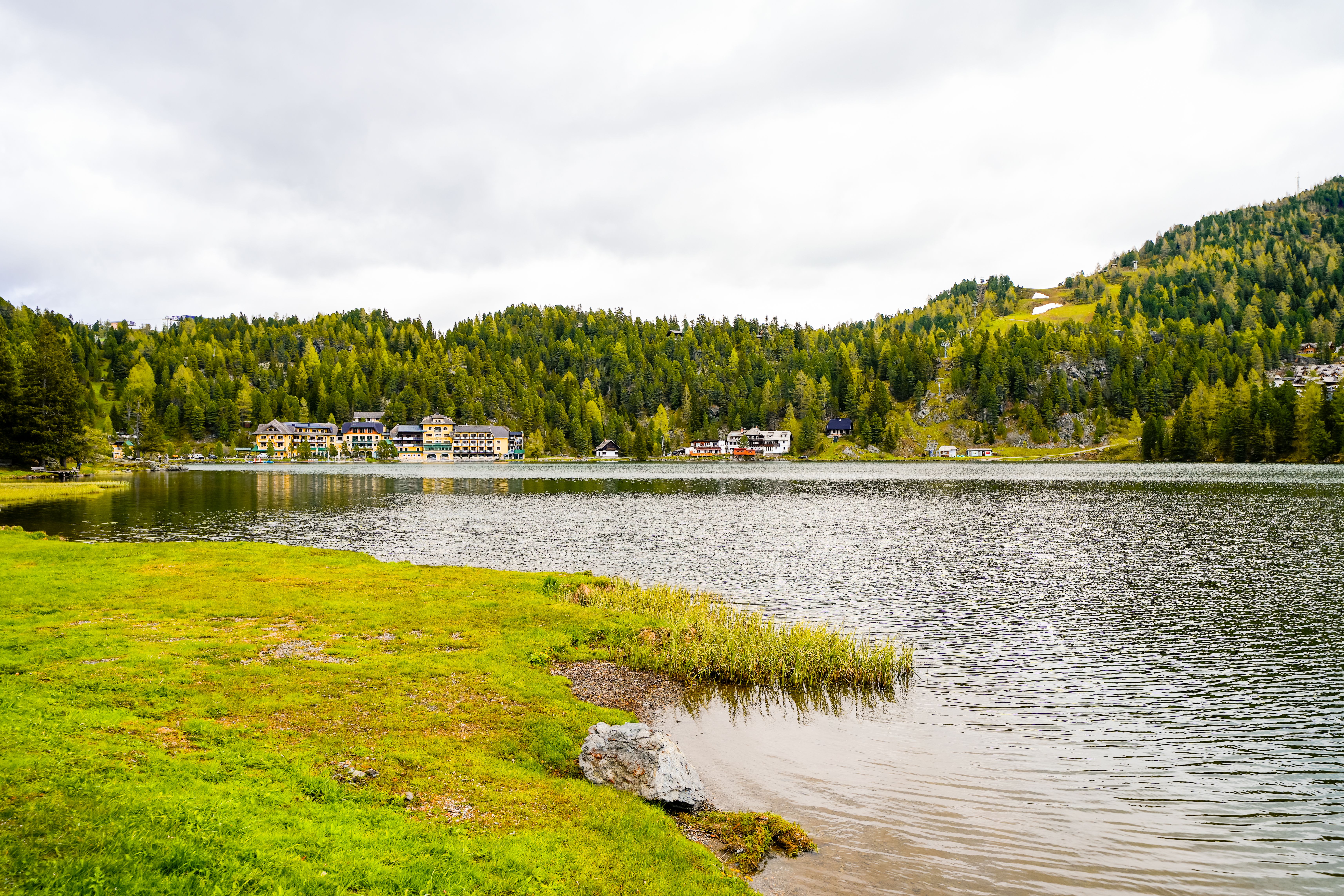 Blick auf den Turracher See mit umliegenden Wäldern und Gebäuden am Ufer.