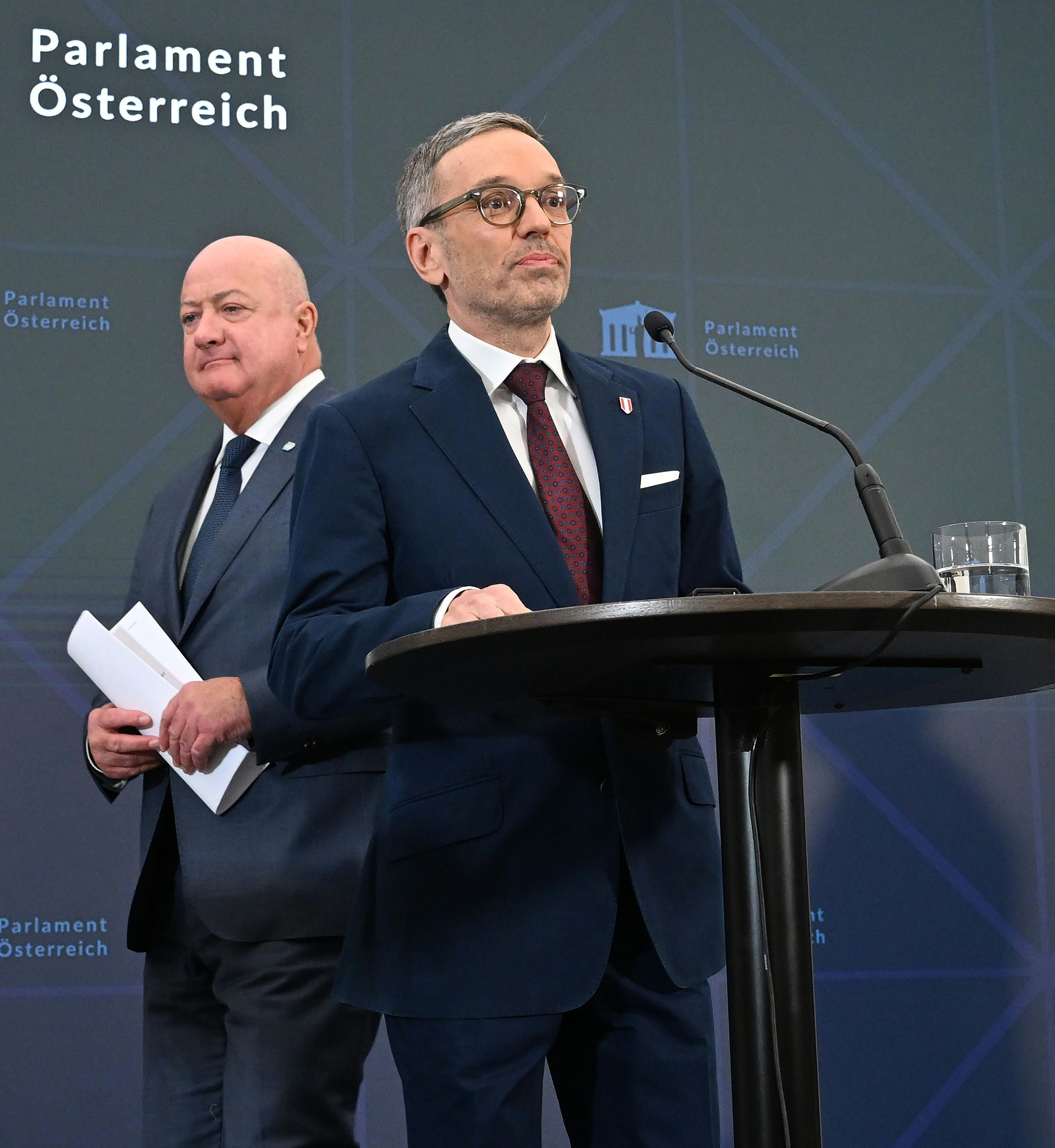 Zwei Männer im Anzug bei einer Pressekonferenz im österreichischen Parlament.