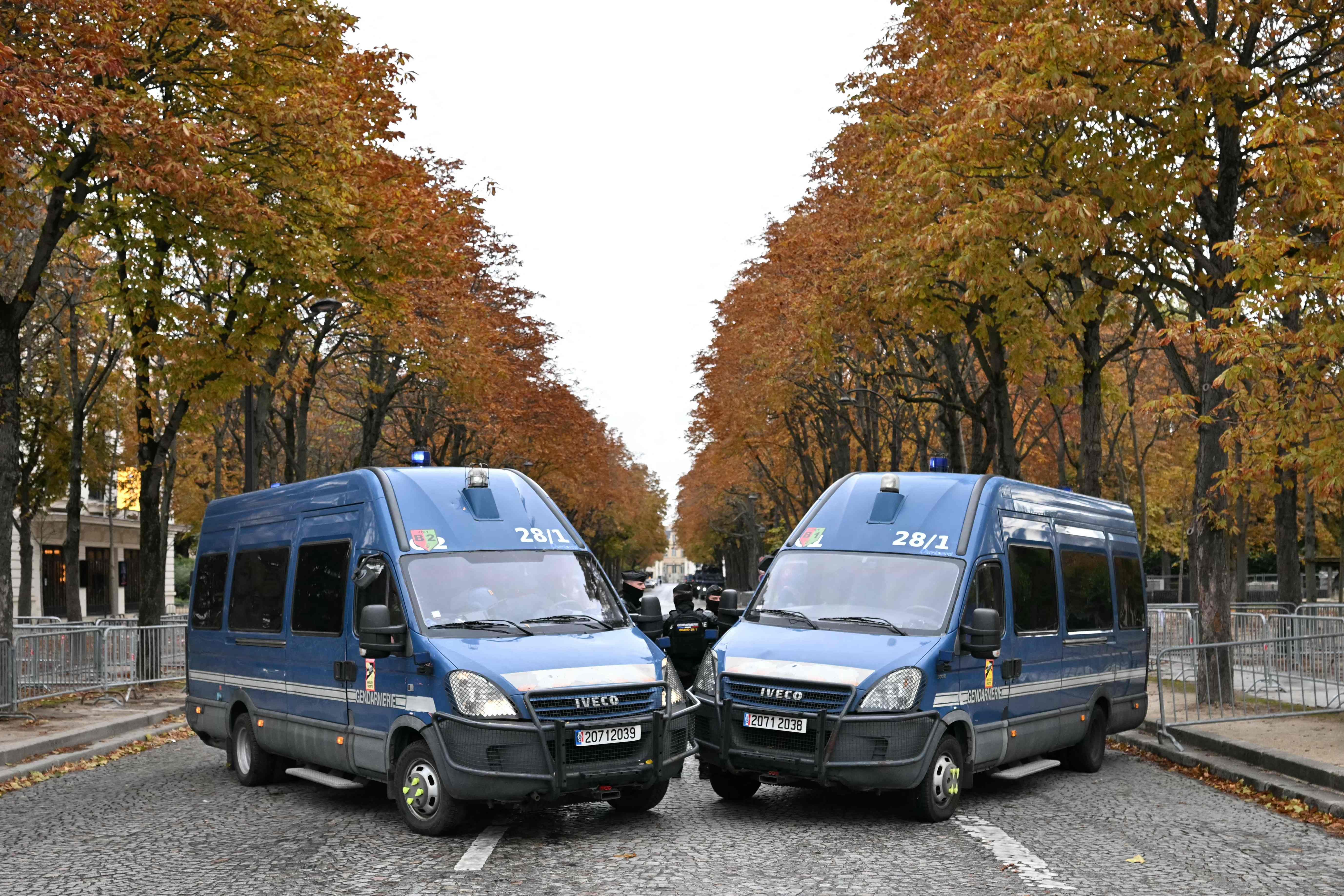 Zwei Einsatzfahrzeuge der Polizei blockieren eine herbstliche Straße in Paris.