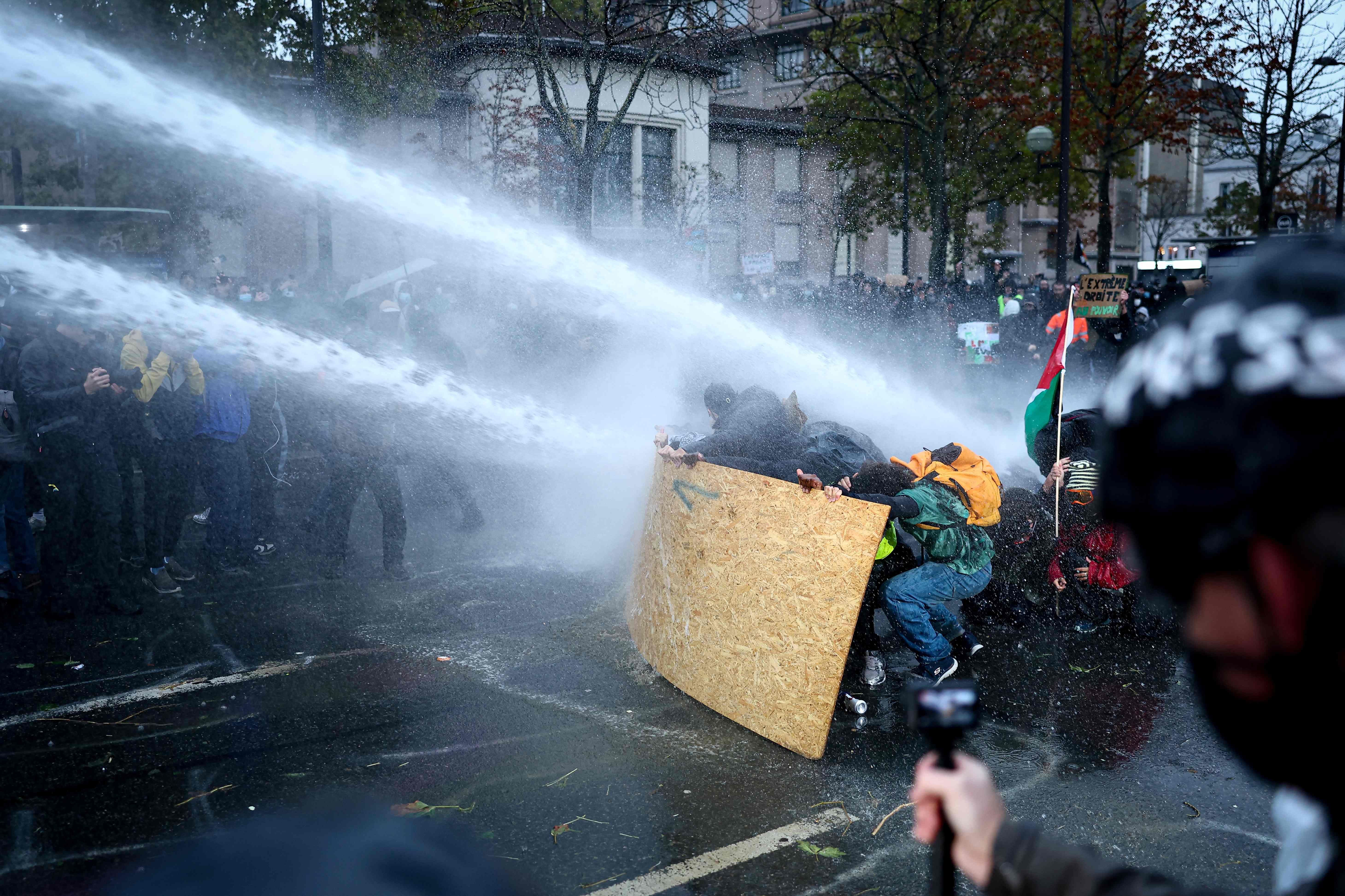 Demonstrierende schützen sich mit einer Holzplatte vor Wasserwerfern bei einem Protest in Paris.