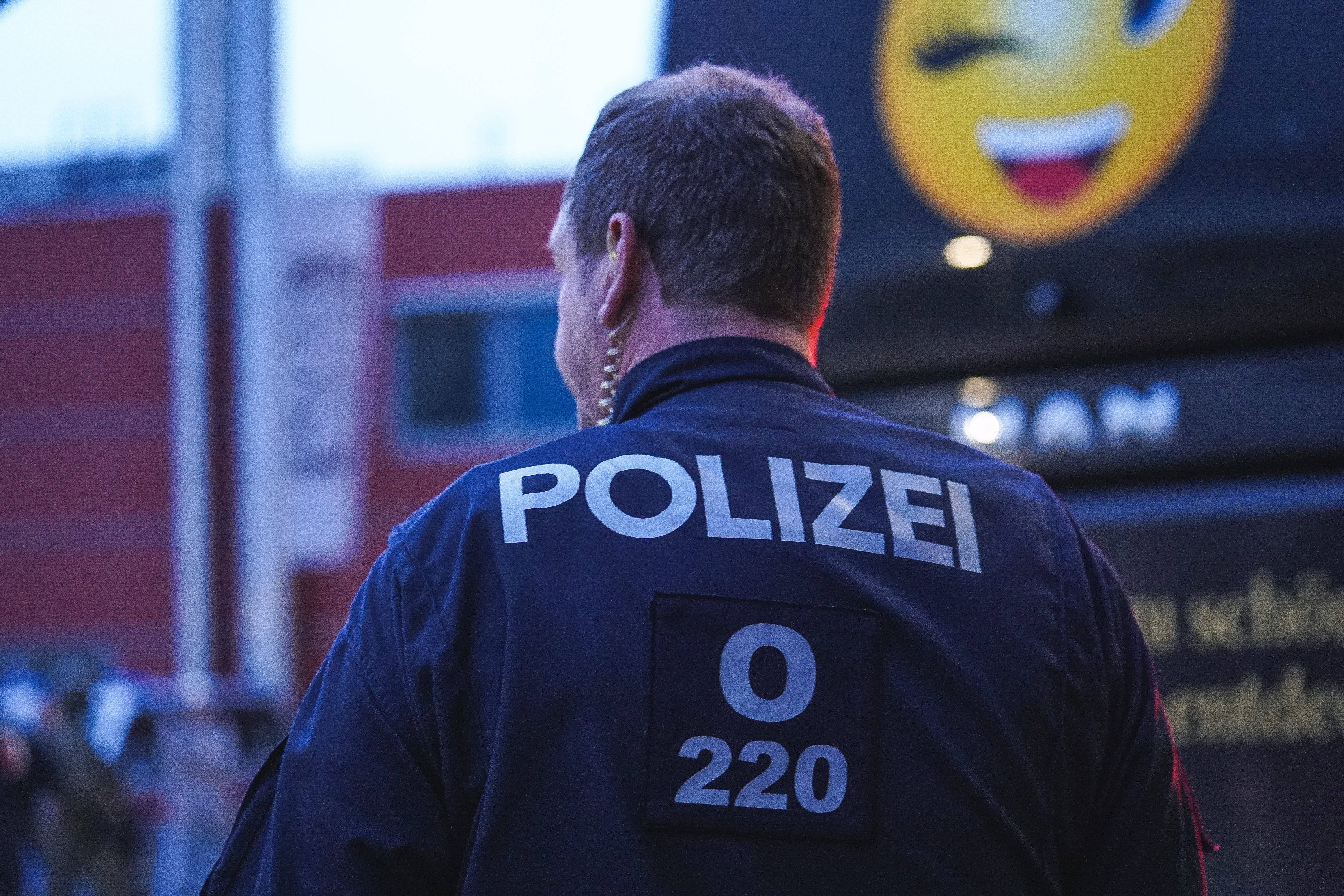 Ein Polizist steht mit dem Rücken zur Kamera, auf seiner Jacke steht "Polizei".