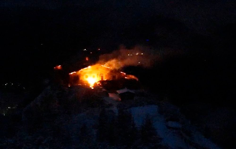 Das Kehlsteinhaus brennt nachts lichterloh, Flammen und Rauch steigen in die Dunkelheit auf.
