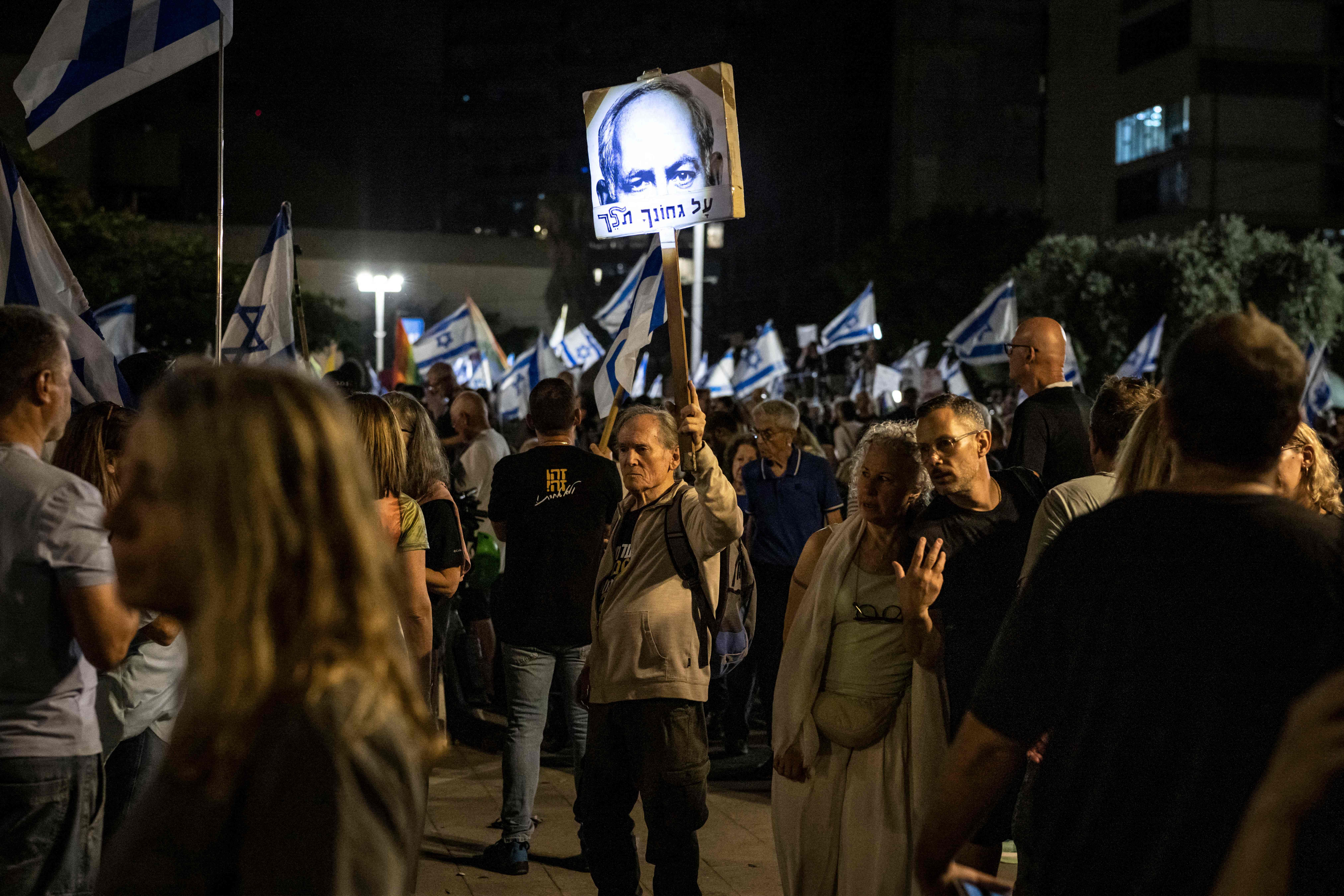 Menschen protestieren nachts in Tel Aviv mit israelischen Flaggen und Plakaten.