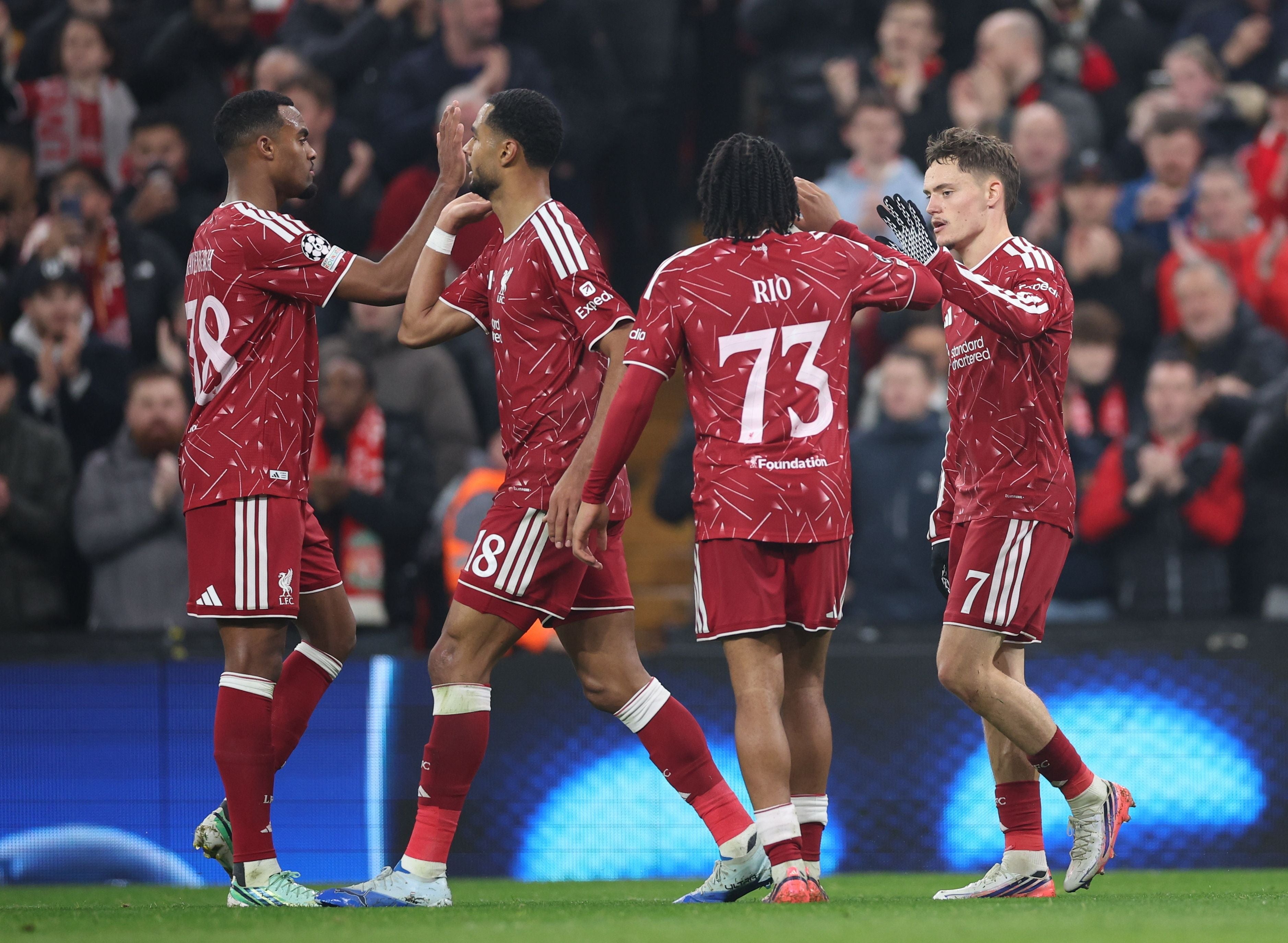 Vier Liverpool-Spieler feiern ein Tor auf dem Fußballfeld vor jubelnden Fans.
