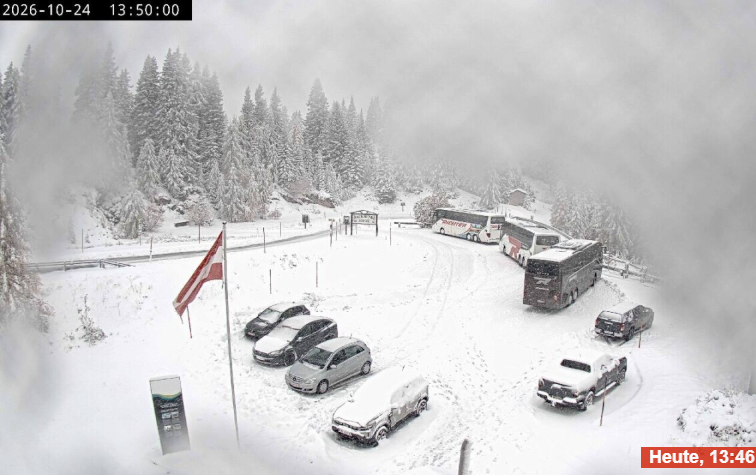 Verschneiter Parkplatz mit Autos, Bussen und einer Fahne, umgeben von schneebedeckten Bäumen.