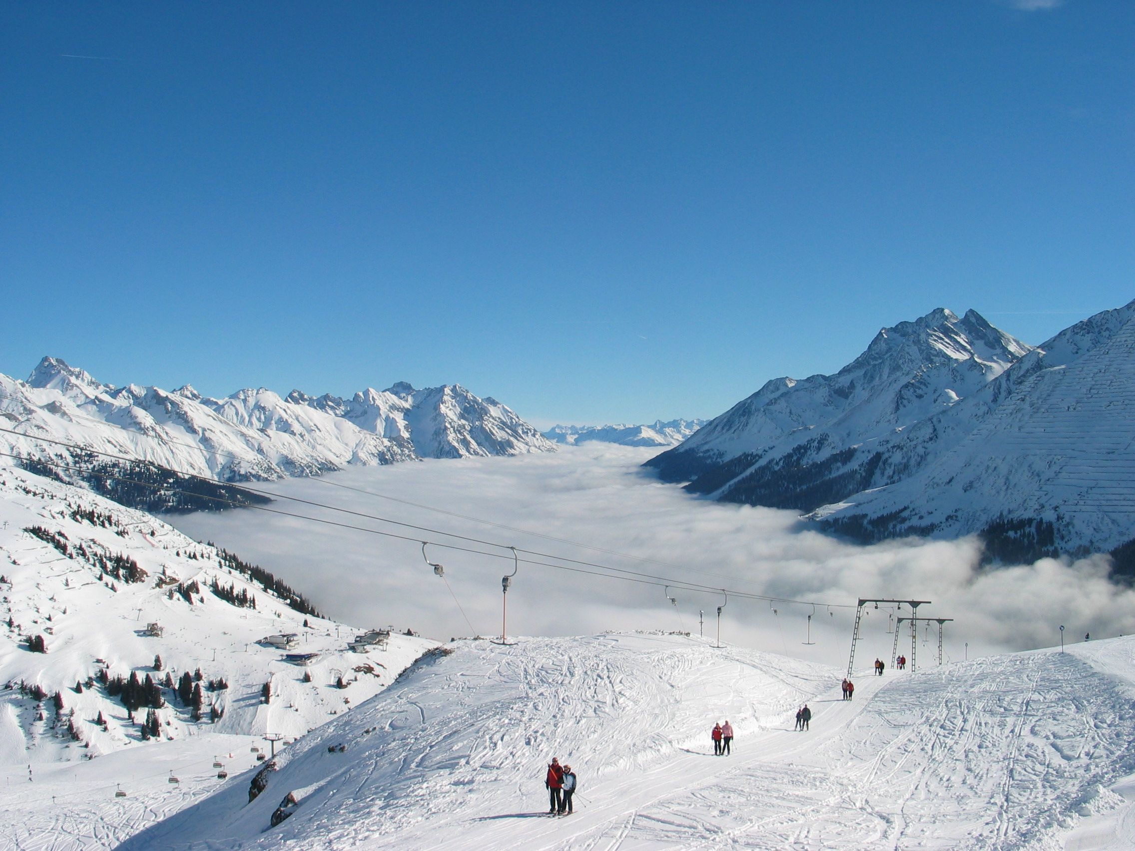 Skifahrer fahren bei Sonnenschein mit dem Skilift in verschneiter Alpenlandschaft bergauf.