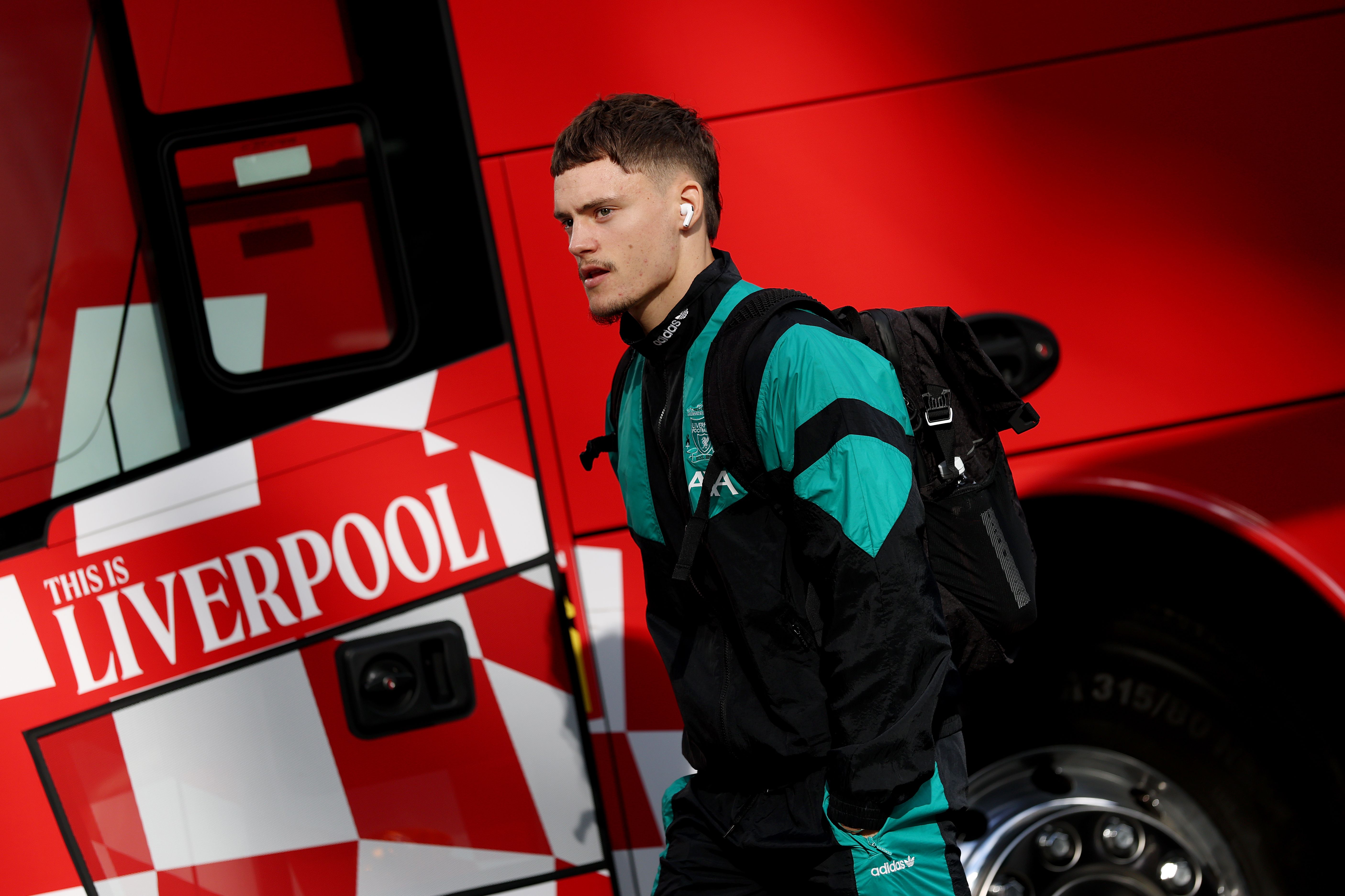 Ein junger Mann in Sportkleidung läuft mit Rucksack vor einem roten Liverpool-Bus entlang.