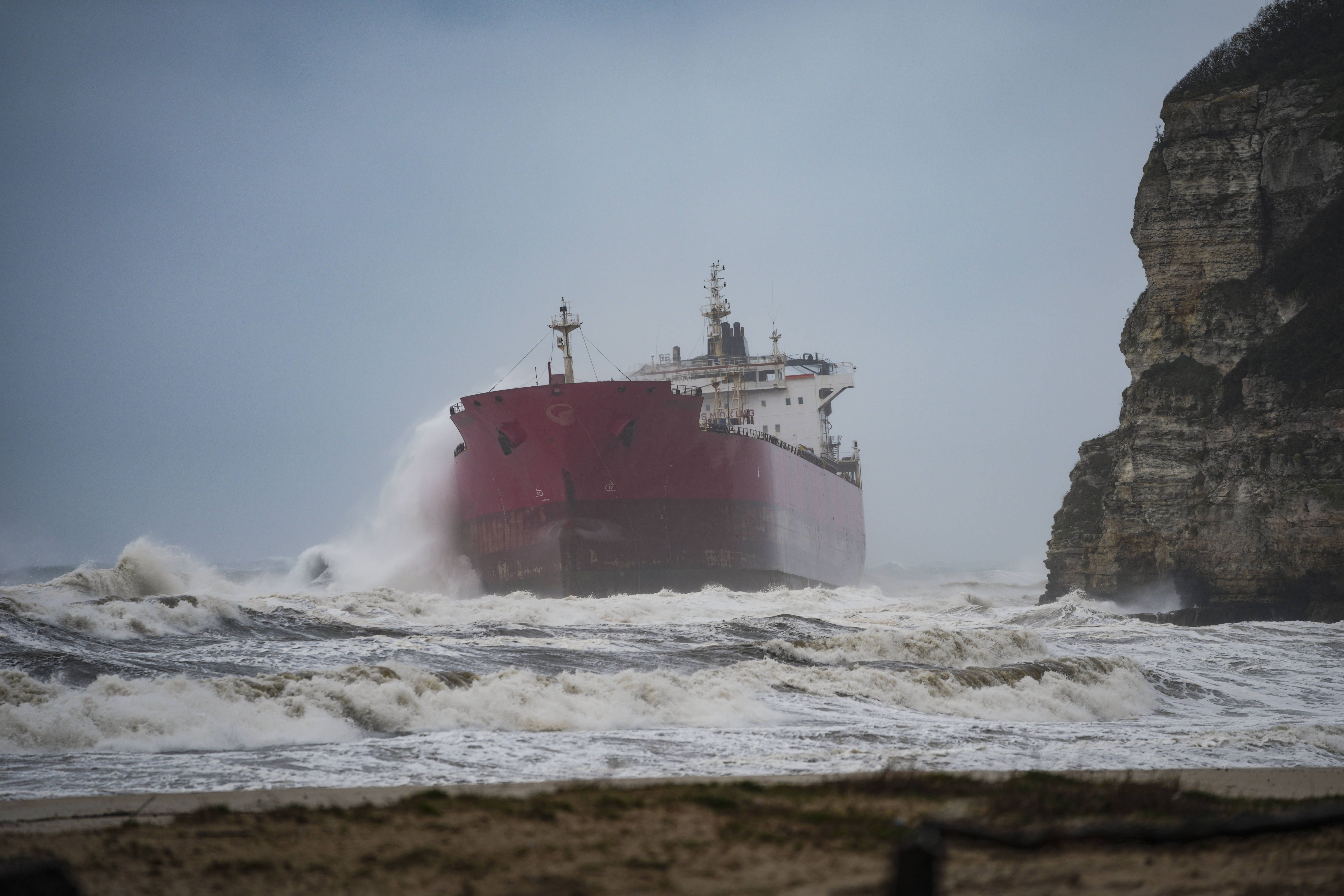 Ein Frachtschiff ist bei stürmischer See nahe einer Felsküste auf Grund gelaufen.