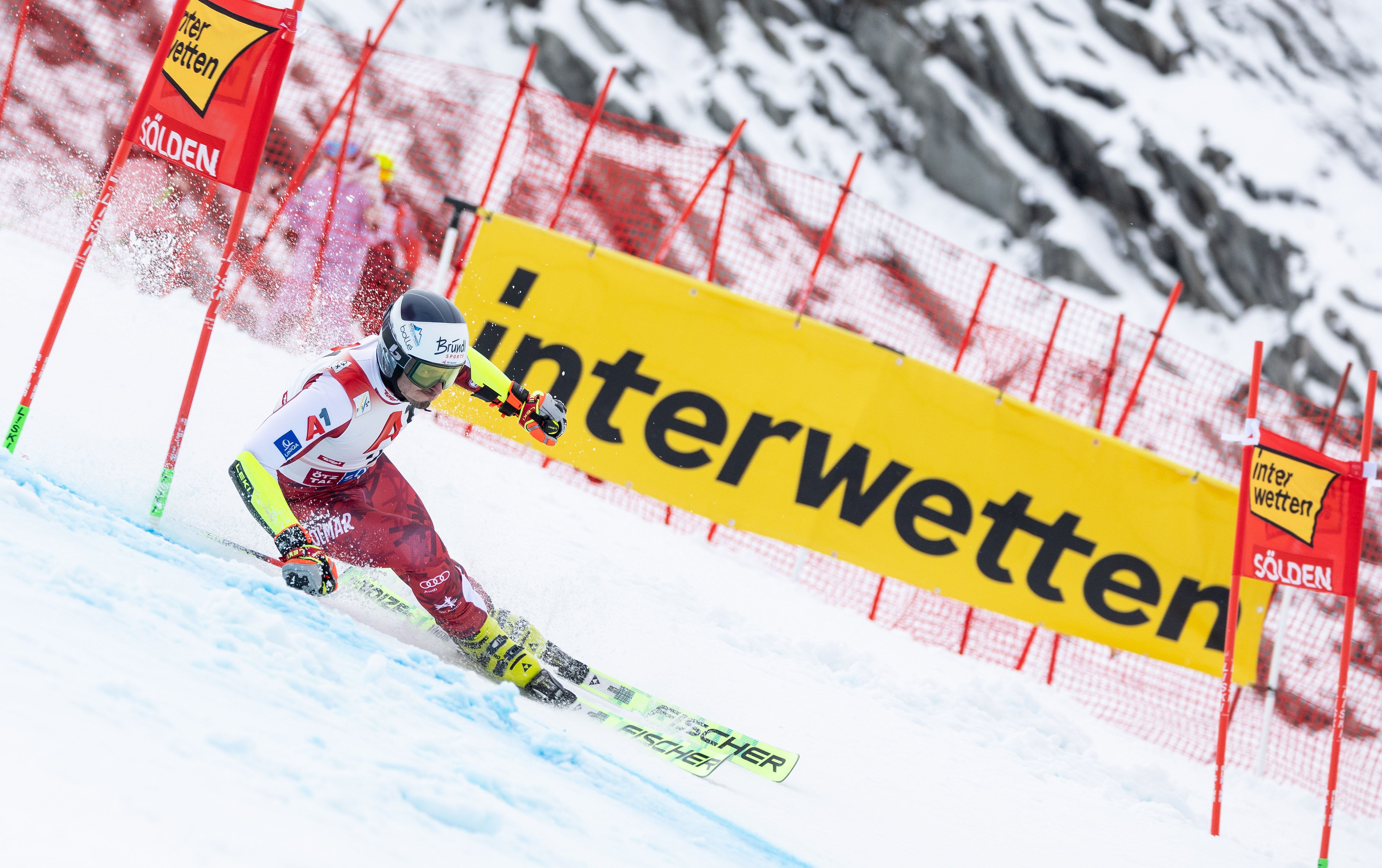 Ein Skirennläufer fährt beim Riesenslalom durch ein Tor im Schnee, im Hintergrund Werbebanner.