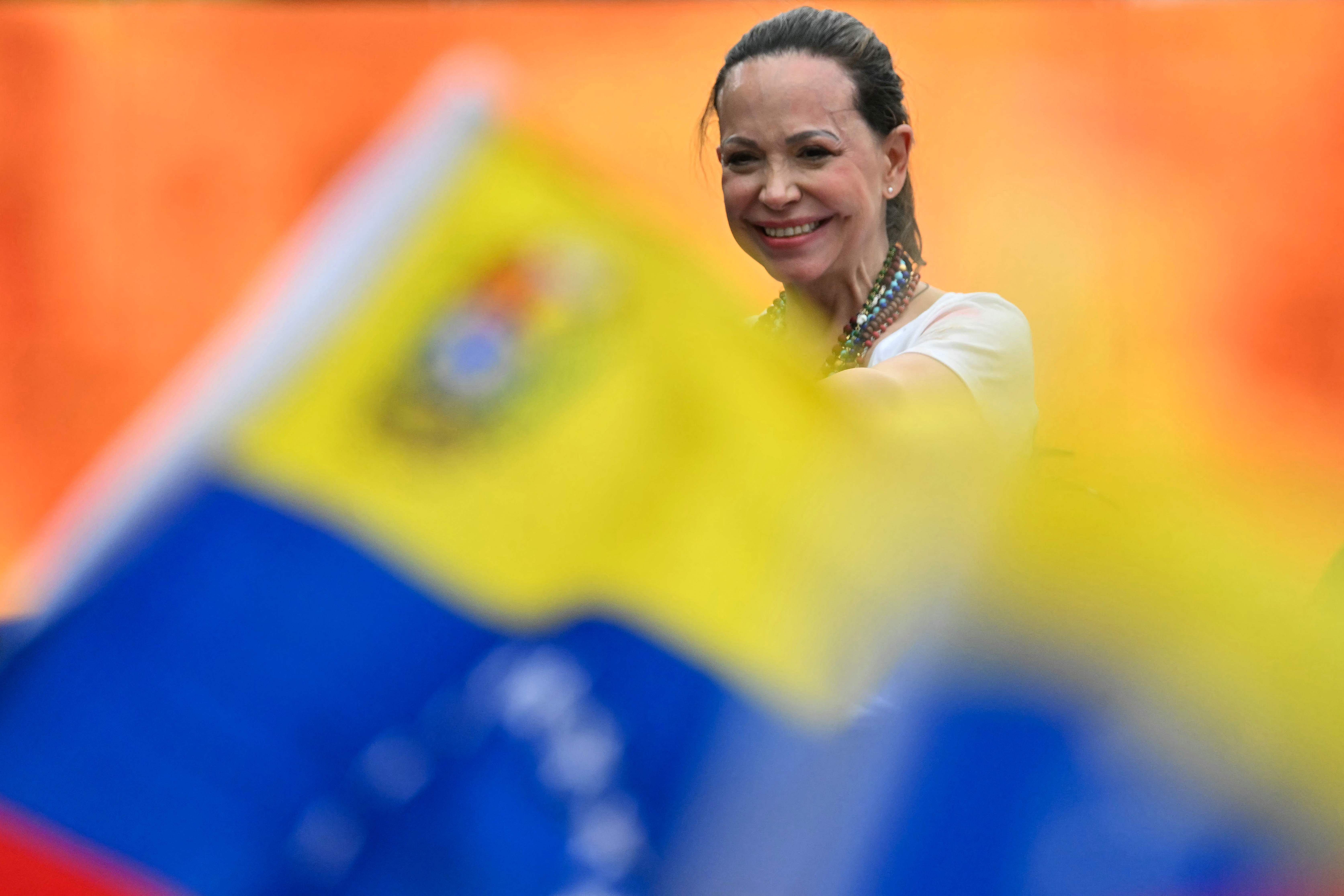 Frau lächelt auf einer Veranstaltung, im Vordergrund sind venezolanische Fahnen zu sehen.