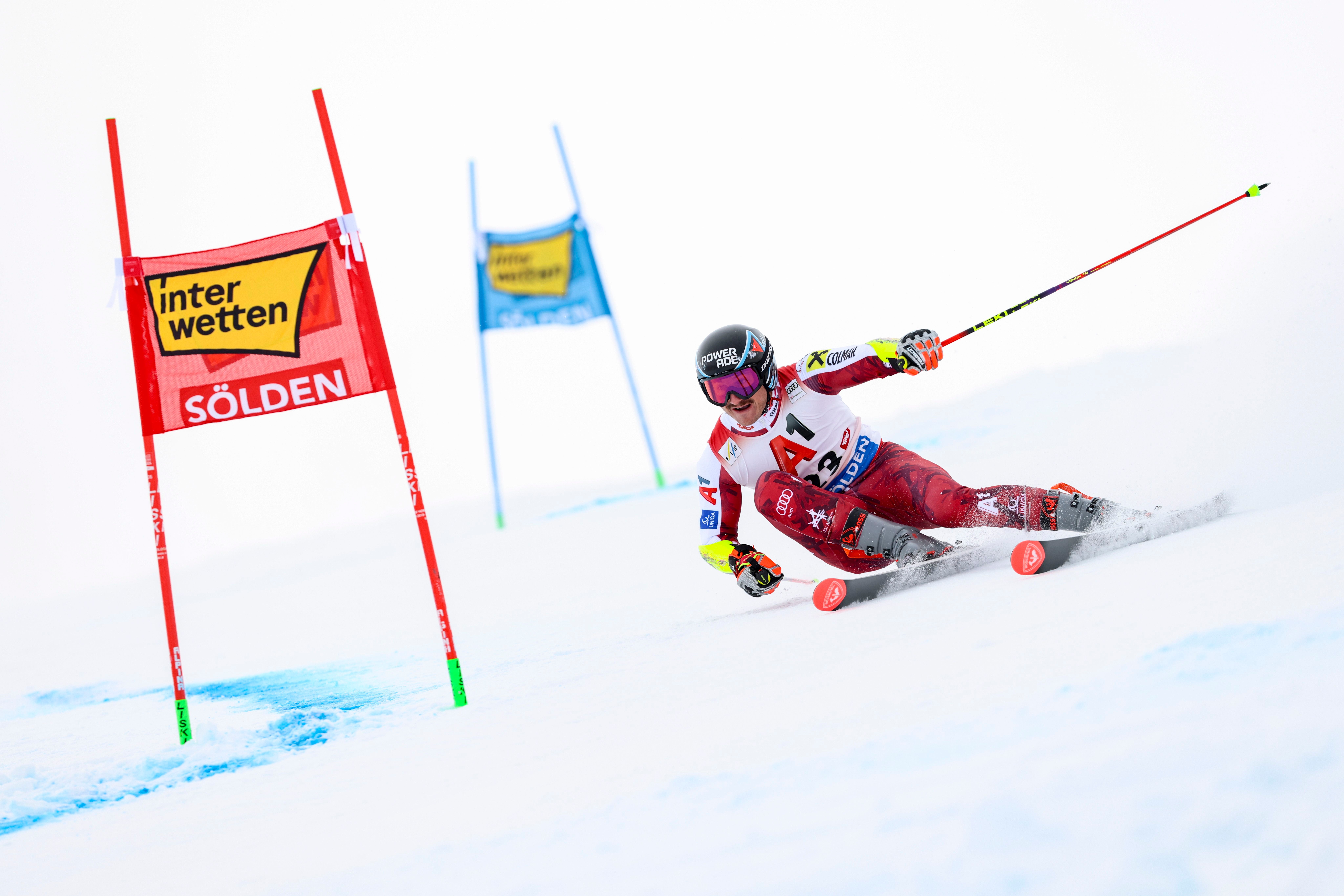 Ein Skirennfahrer fährt im Riesenslalom zwischen Torstangen auf einer schneebedeckten Piste.