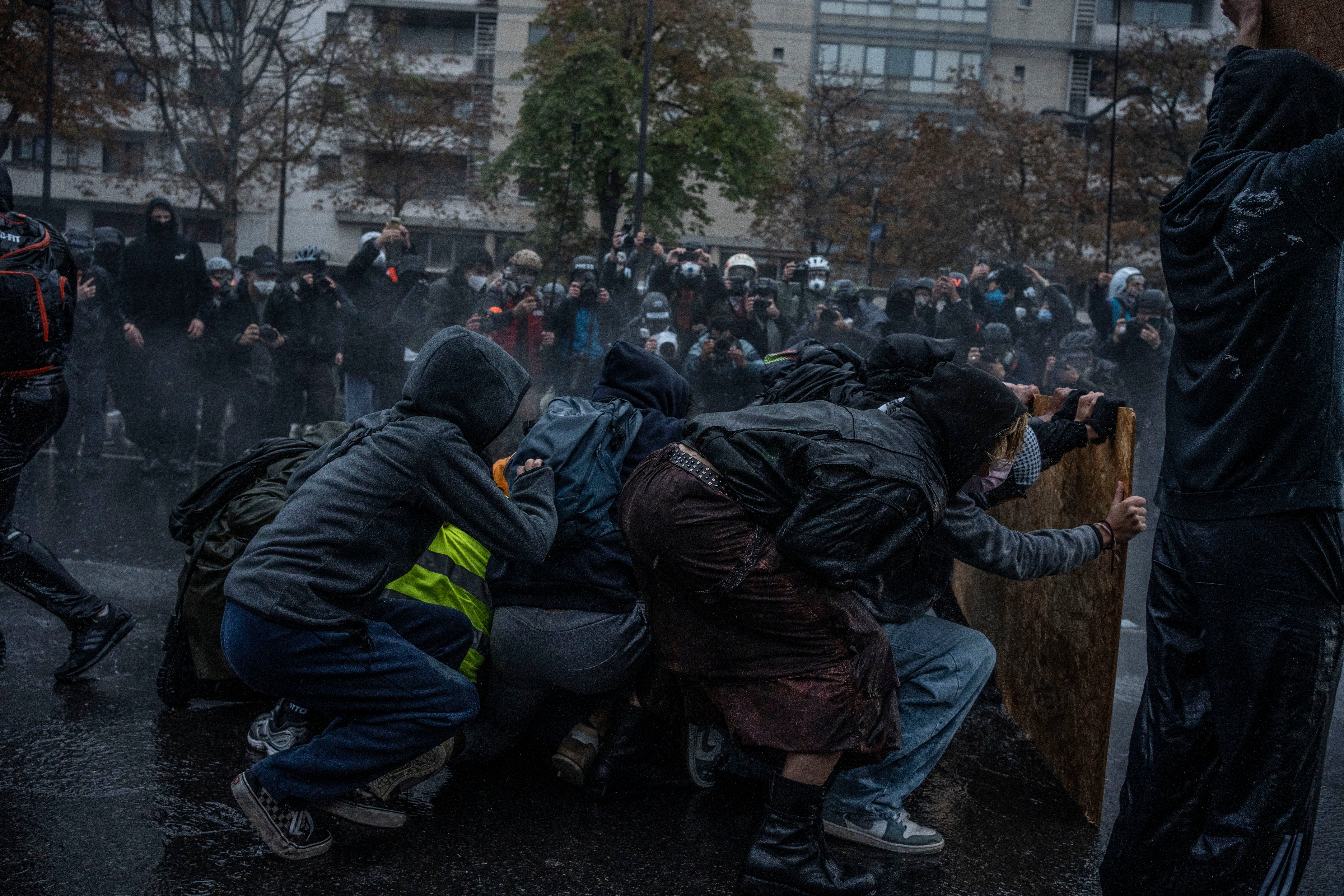 Demonstranten ducken sich mit Schild vor Wasserwerfer während Protesten auf einer Pariser Straße.