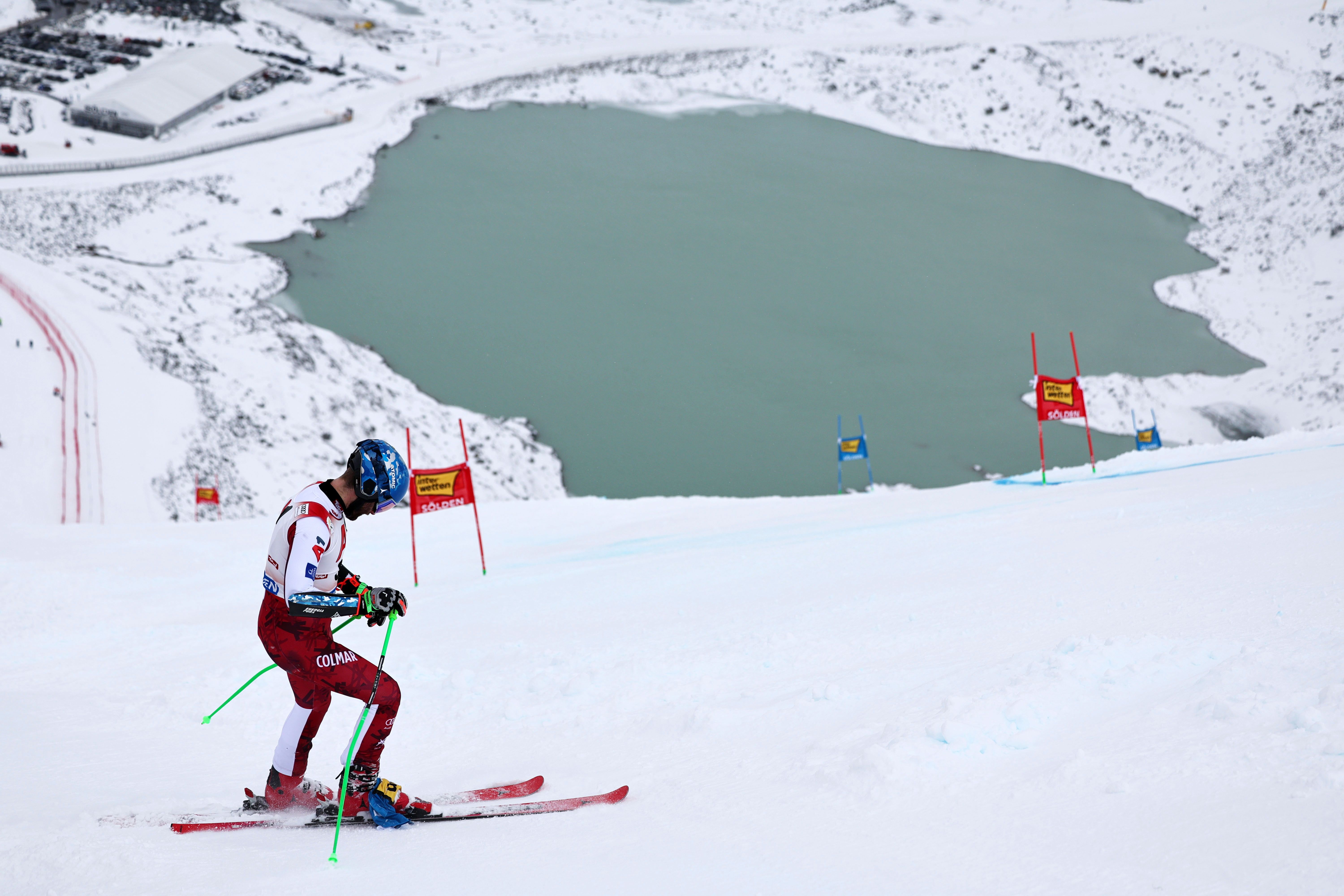 Ein Skifahrer auf einer verschneiten Piste mit Toren, im Hintergrund ein See und schneebedeckte Berge.