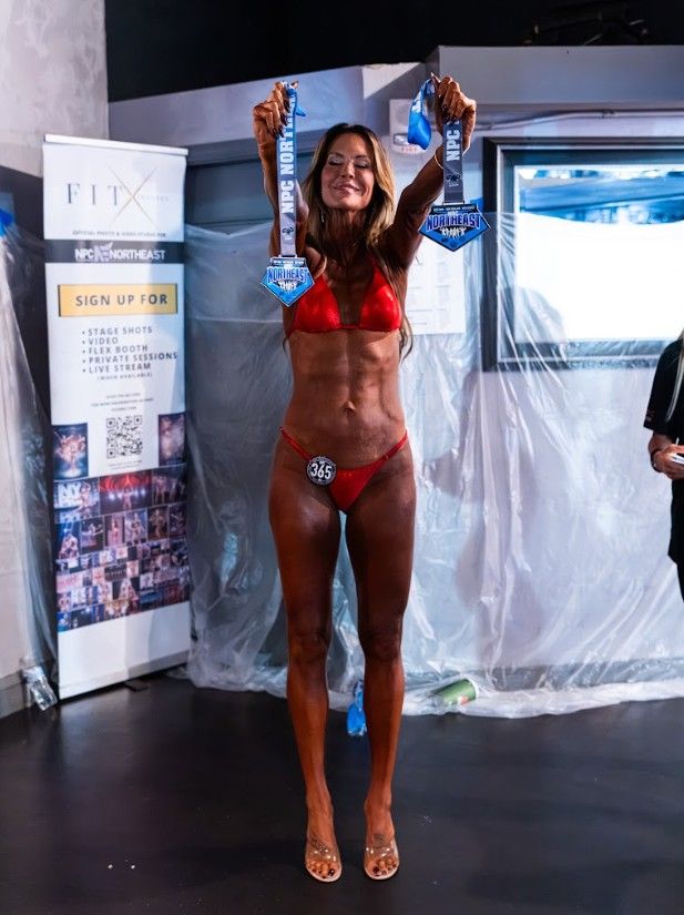 Frau im roten Bikini hält Gewinner-Medaillen bei einem Bodybuilding-Wettbewerb hoch.