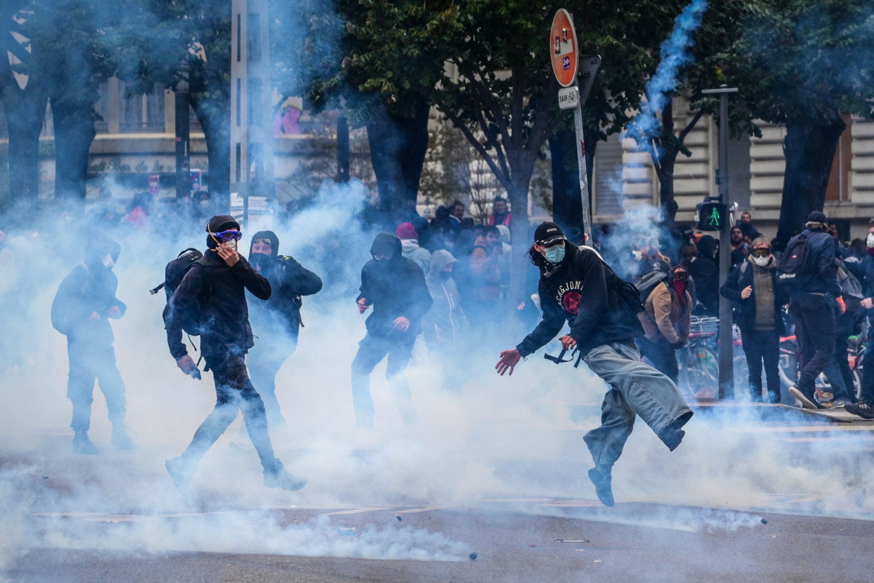 Demonstranten stoßen in Lyon durch Tränengas, einige treten Gaskanister weg, viele mit Masken geschützt.