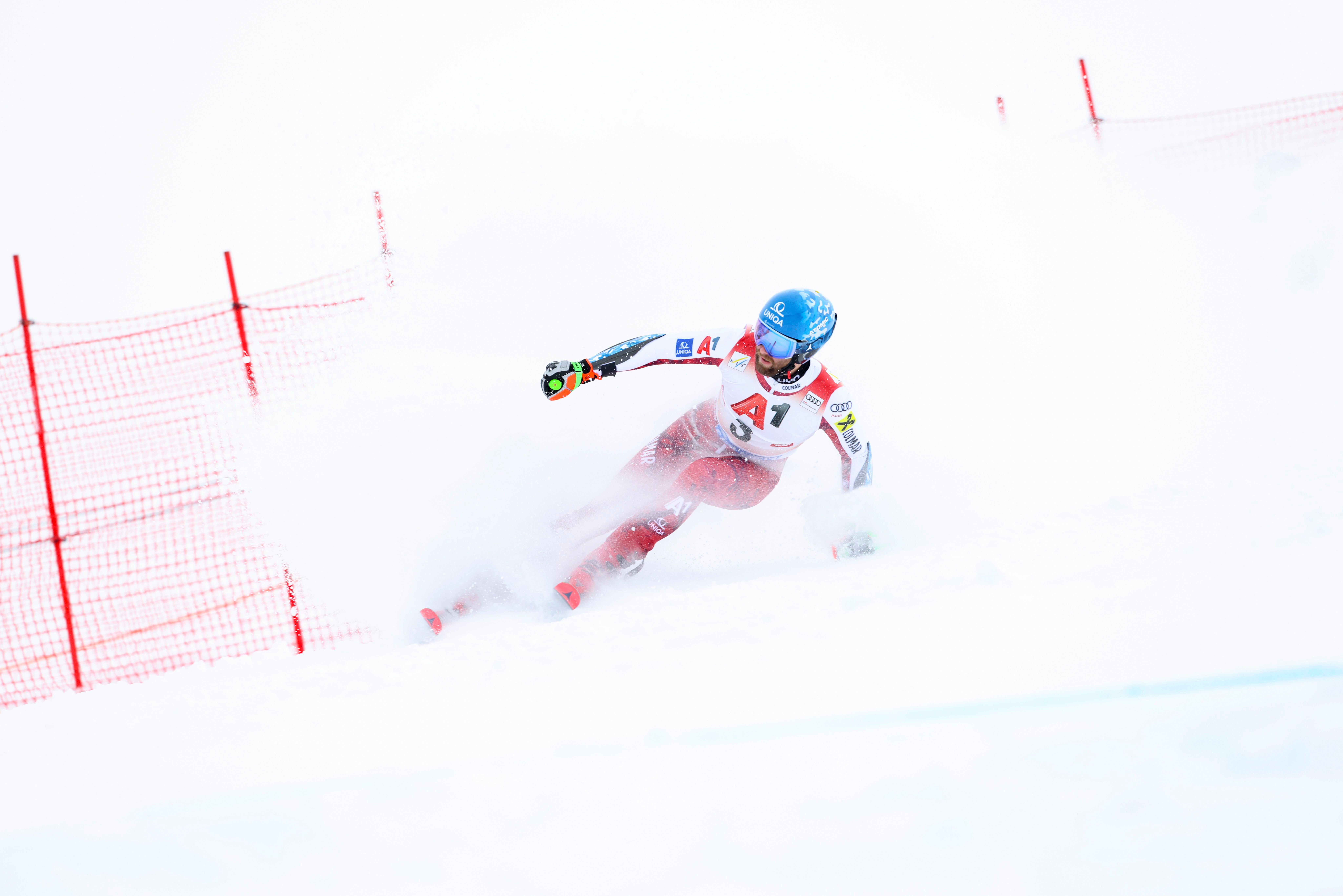 Ein Skirennläufer fährt beim Riesenslalom durch eine Kurve und wirbelt Schnee auf.
