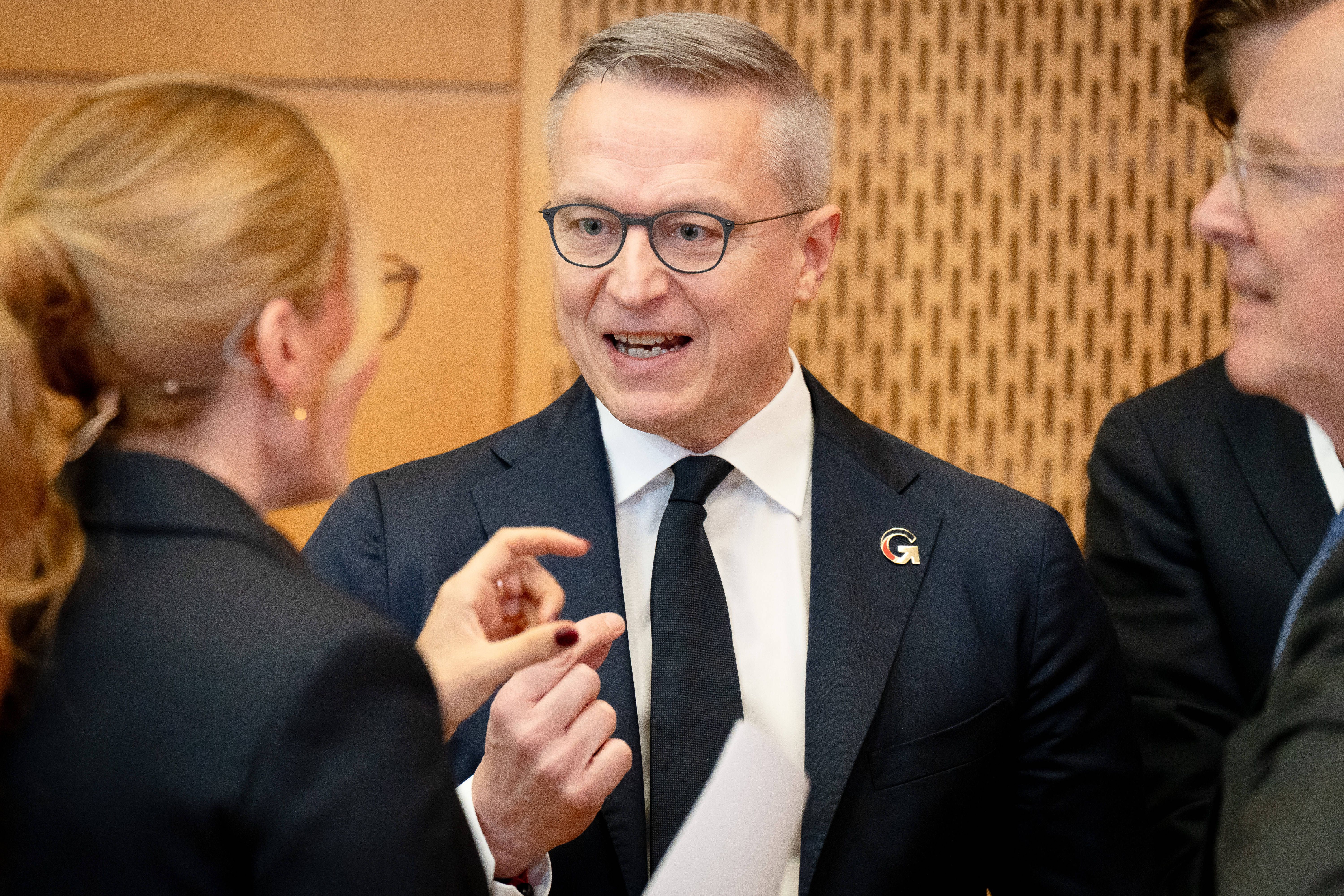 Ein Mann im Anzug spricht lebhaft mit zwei weiteren Personen auf einer Konferenz.