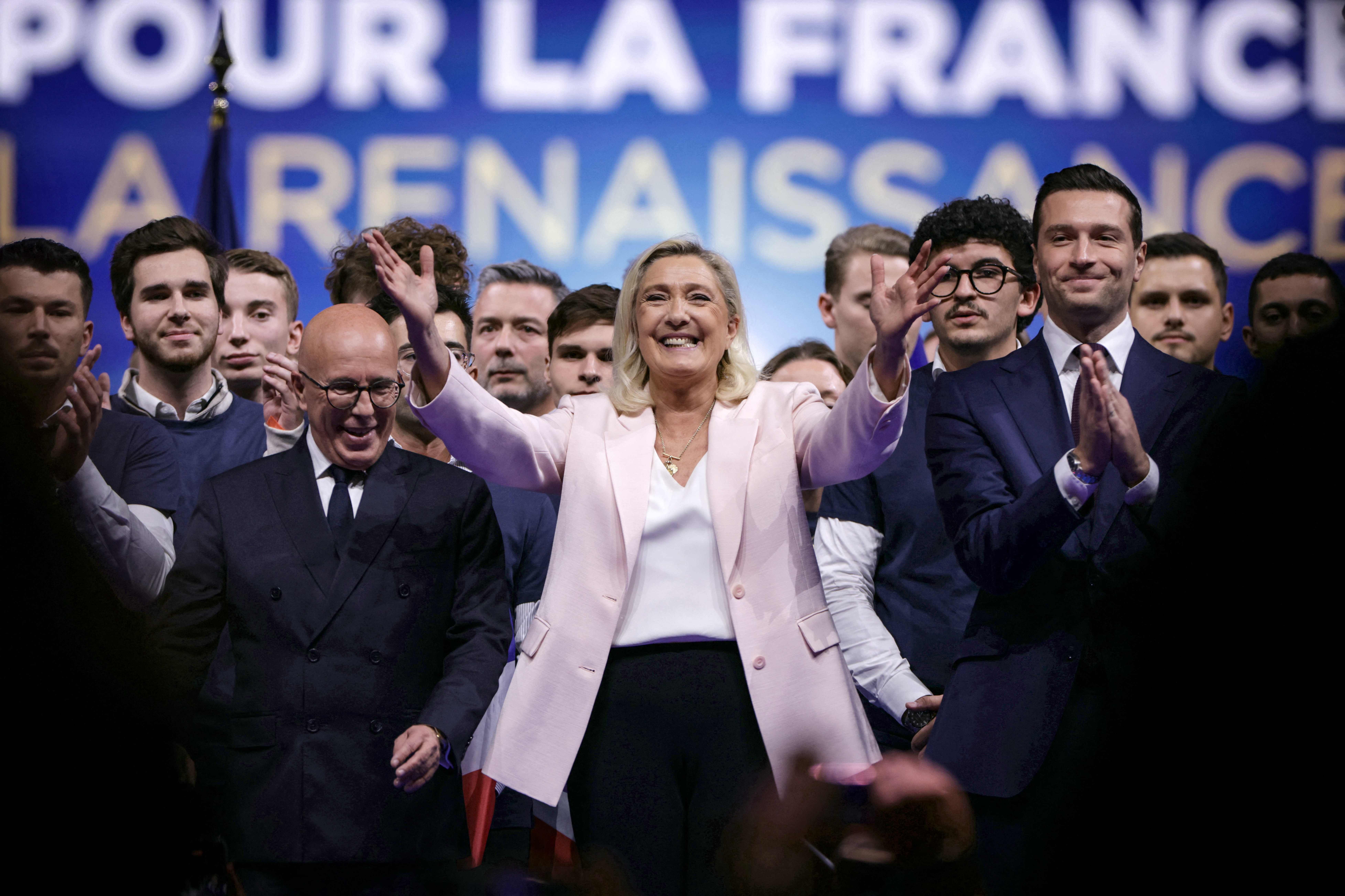 Marine Le Pen steht jubelnd mit Parteikollegen auf einer Bühne vor einer Menschenmenge.