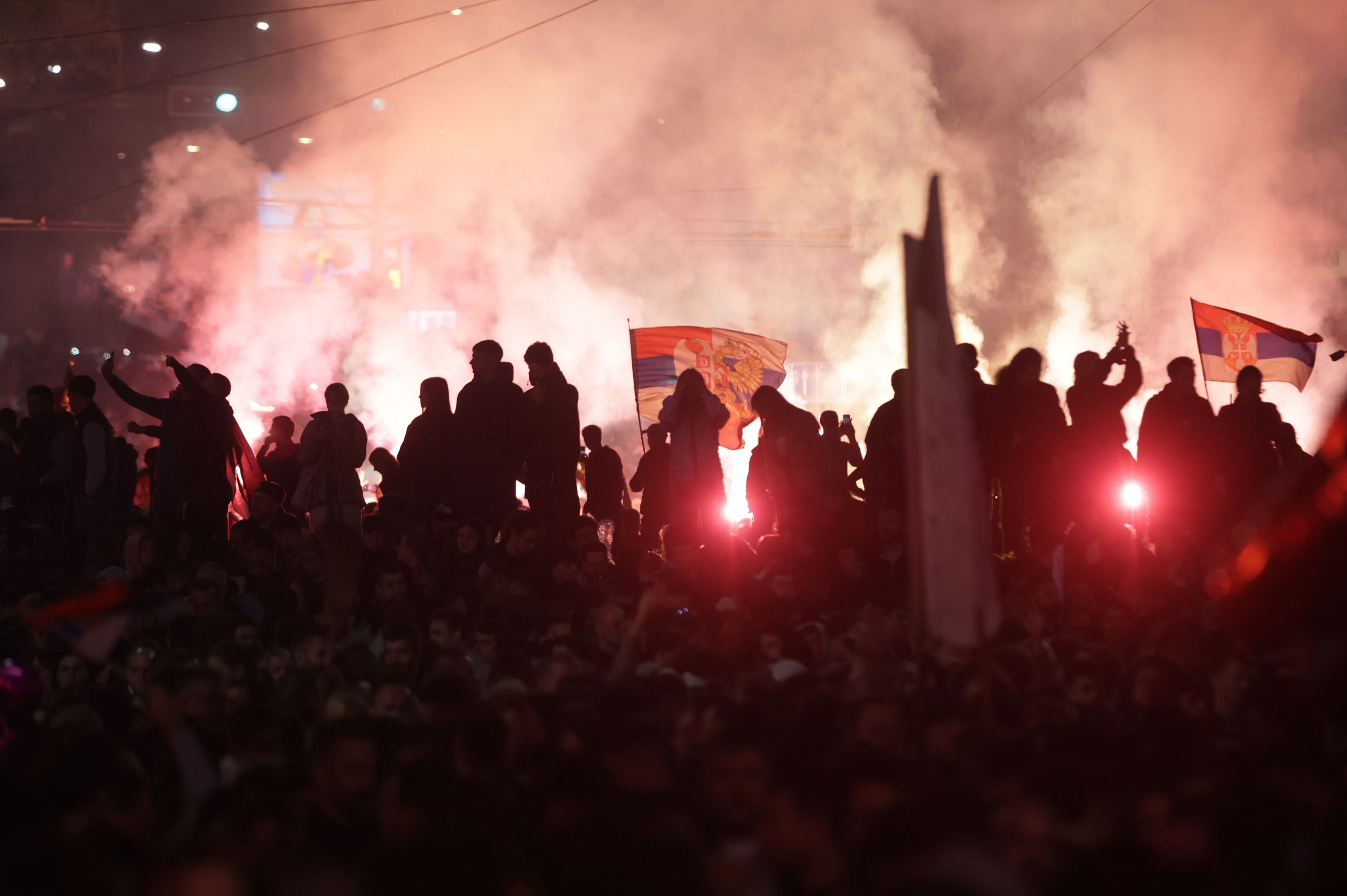Menschenmenge mit serbischen Fahnen und Rauch feiert bei Nacht nach der Wahl in Belgrad.