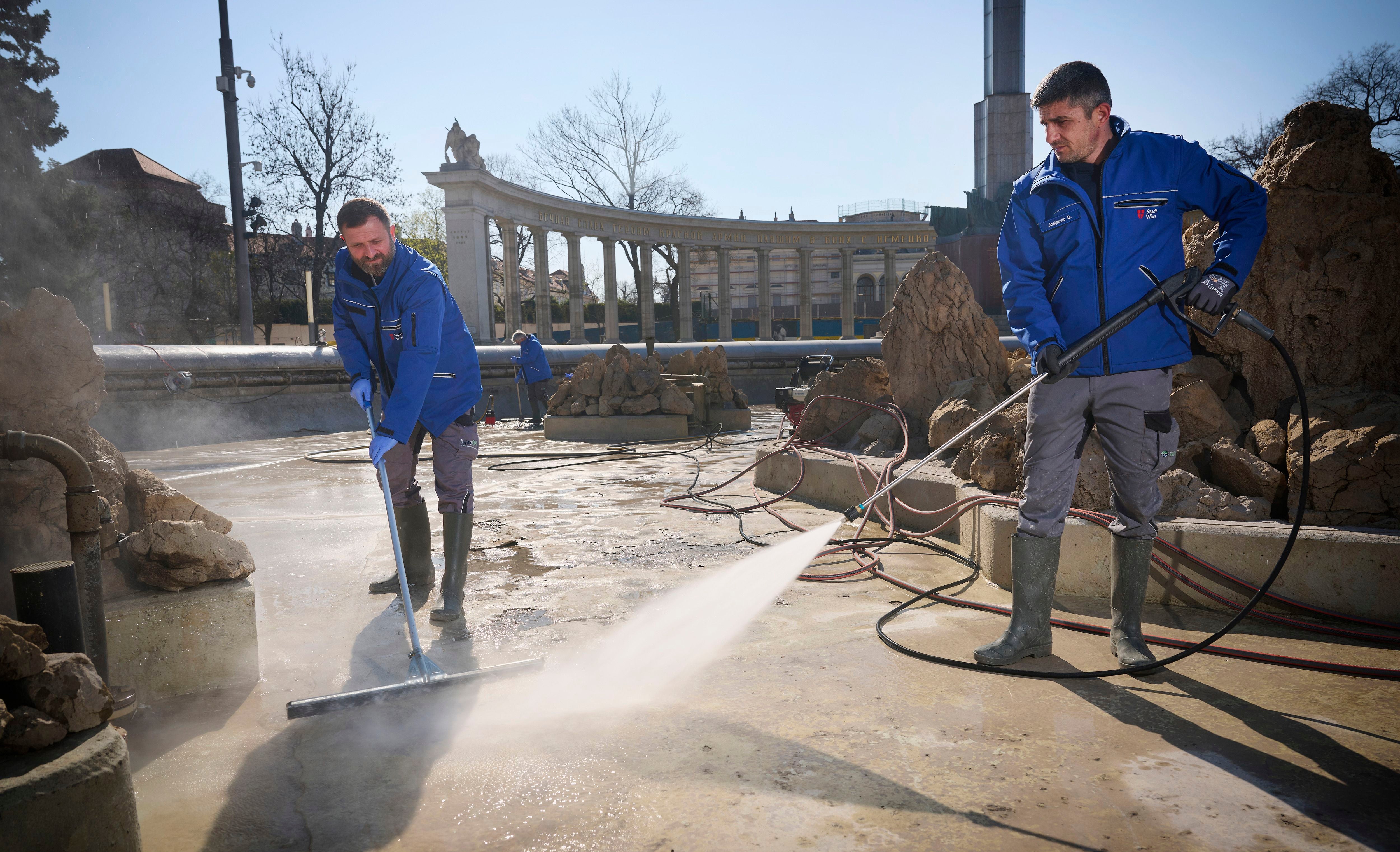 Zwei Männer reinigen den Hochstrahlbrunnen mit Hochdruckreiniger und Schieber.